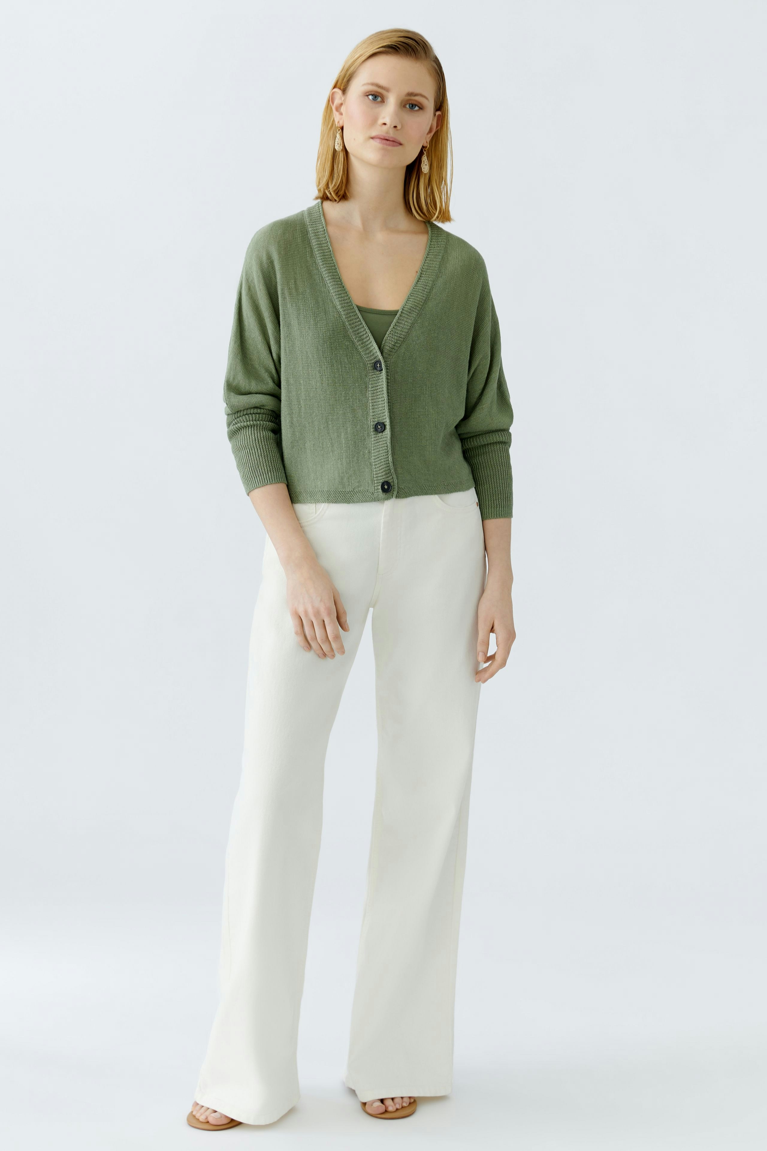 Elegante Damen-Strickjacke in sanftem Grün, lässig kombiniert mit hellen Hosen.