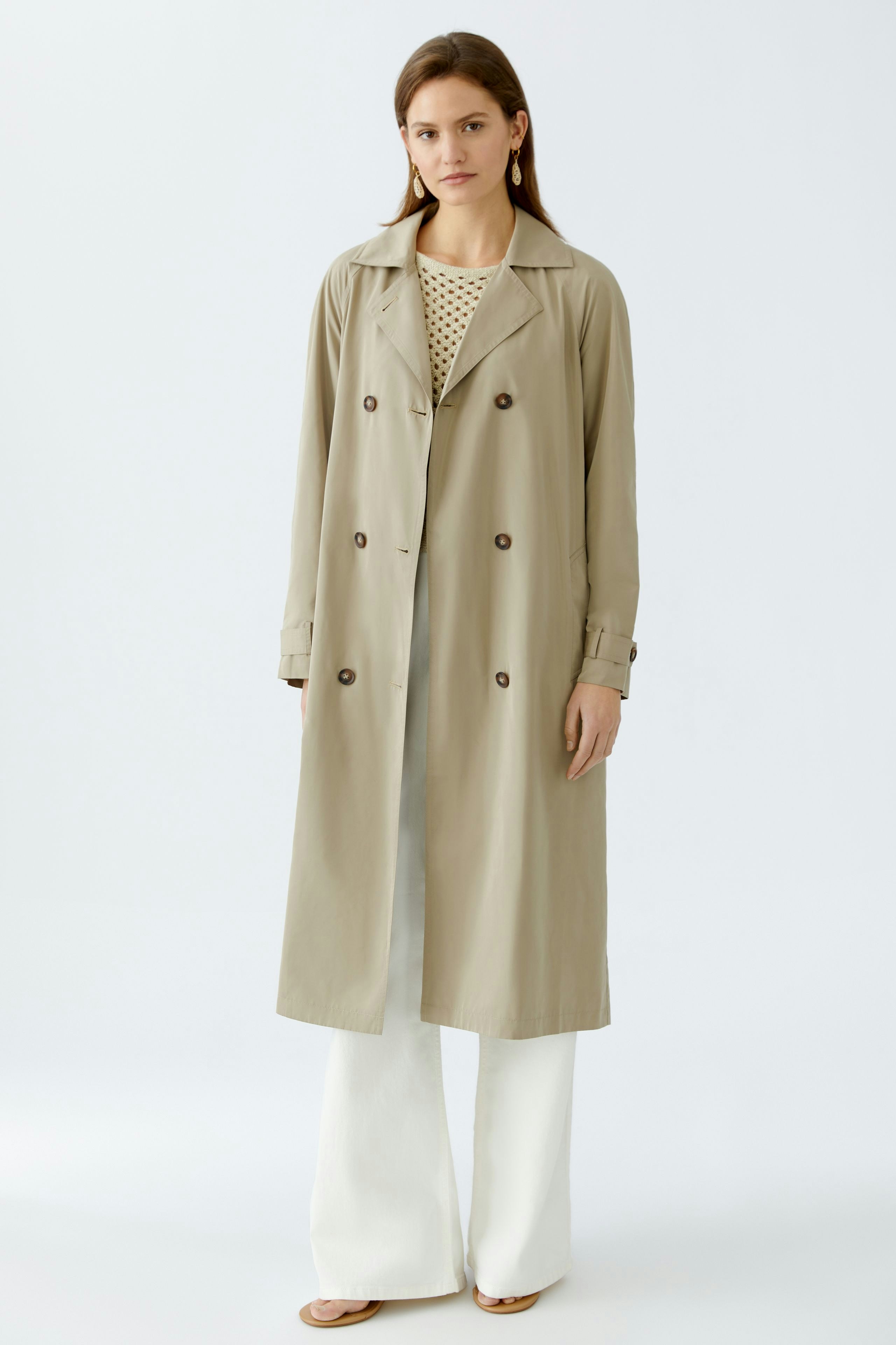 Stylish trench coat: A woman in a beige trench coat over a polka dot top, exuding elegance.