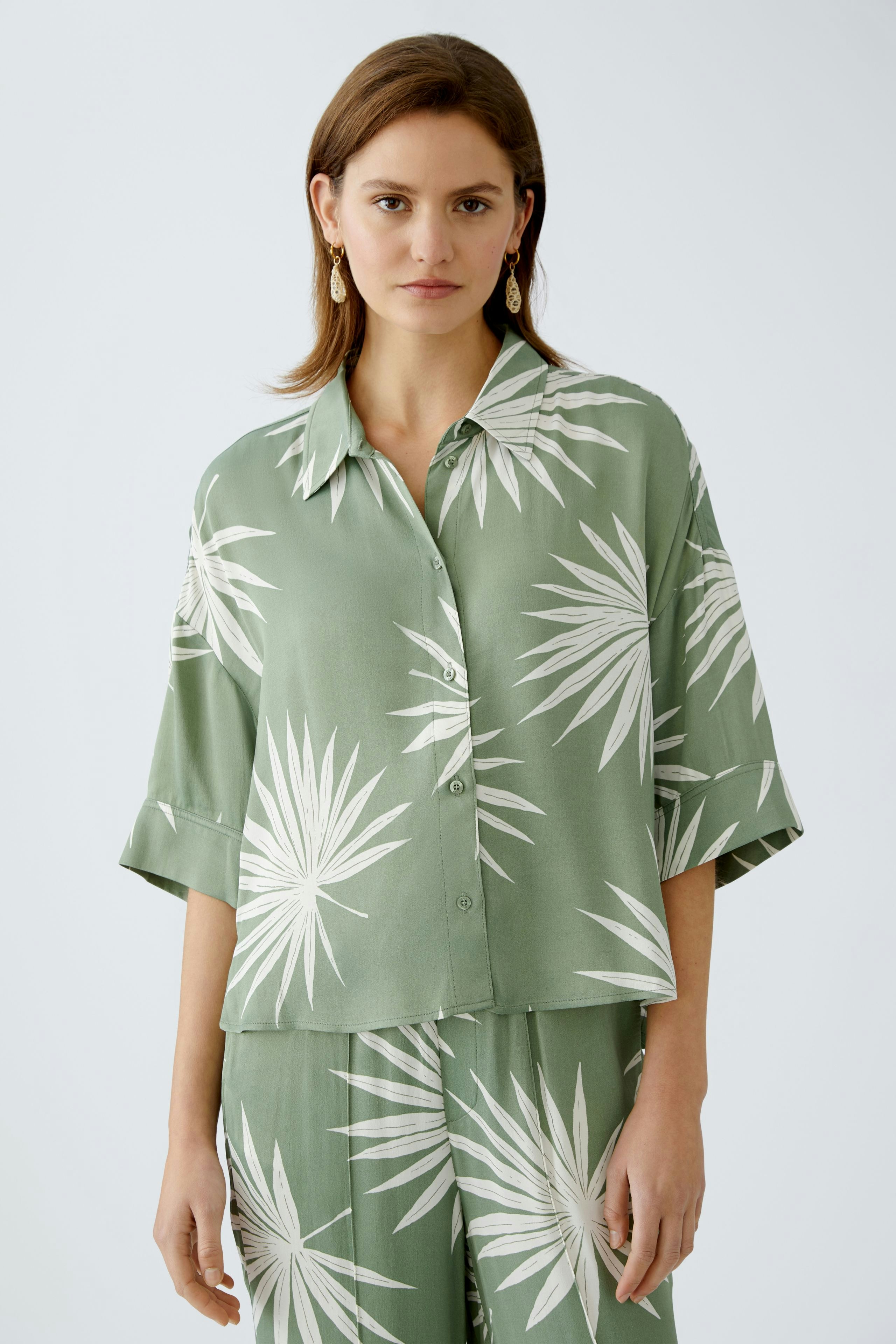 Stylish women's blouse: A woman in a green blouse with a palm leaf print, exuding a relaxed vibe.