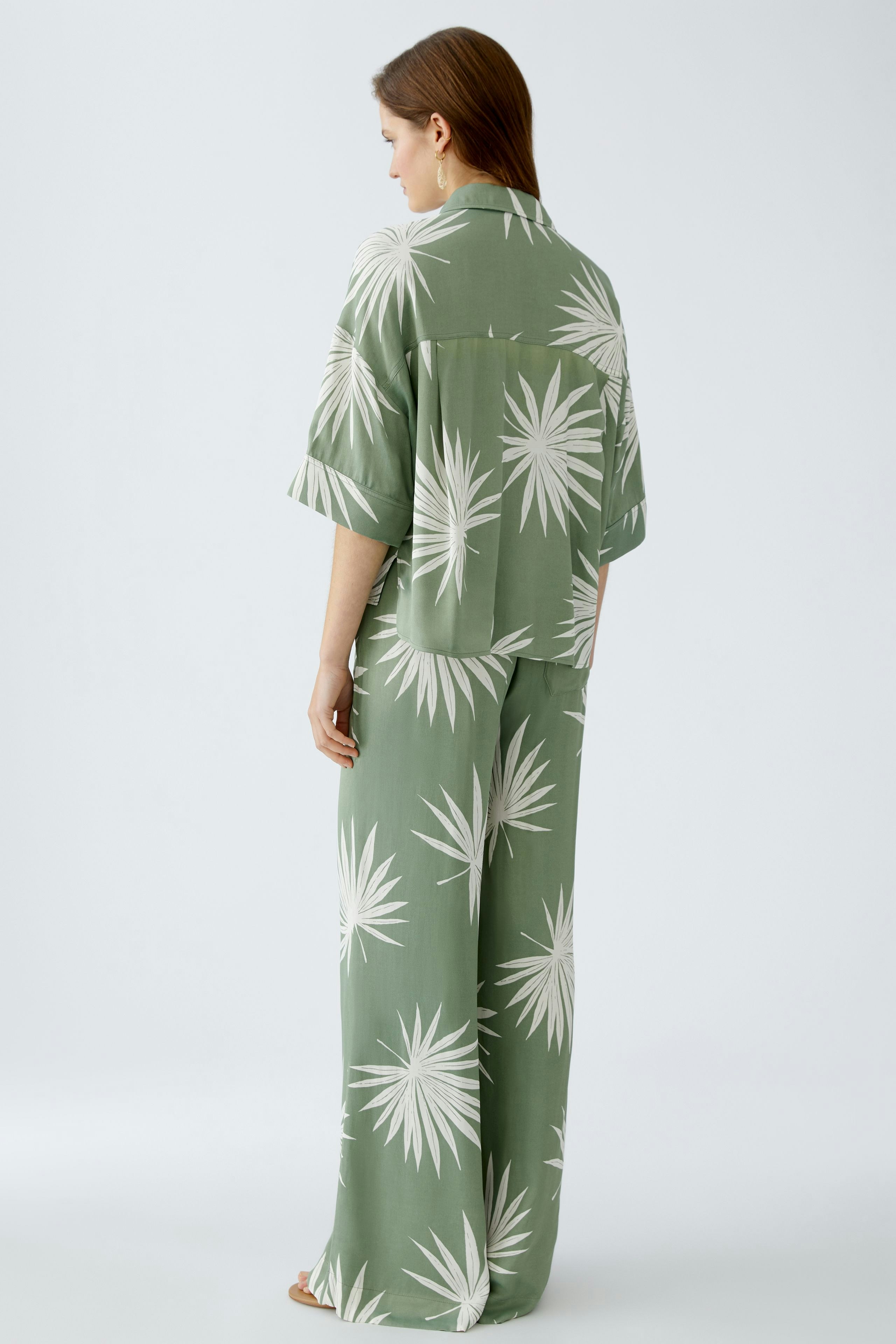 Stylish women's blouse: A woman in a green blouse with a palm leaf pattern, showcasing a relaxed fit.