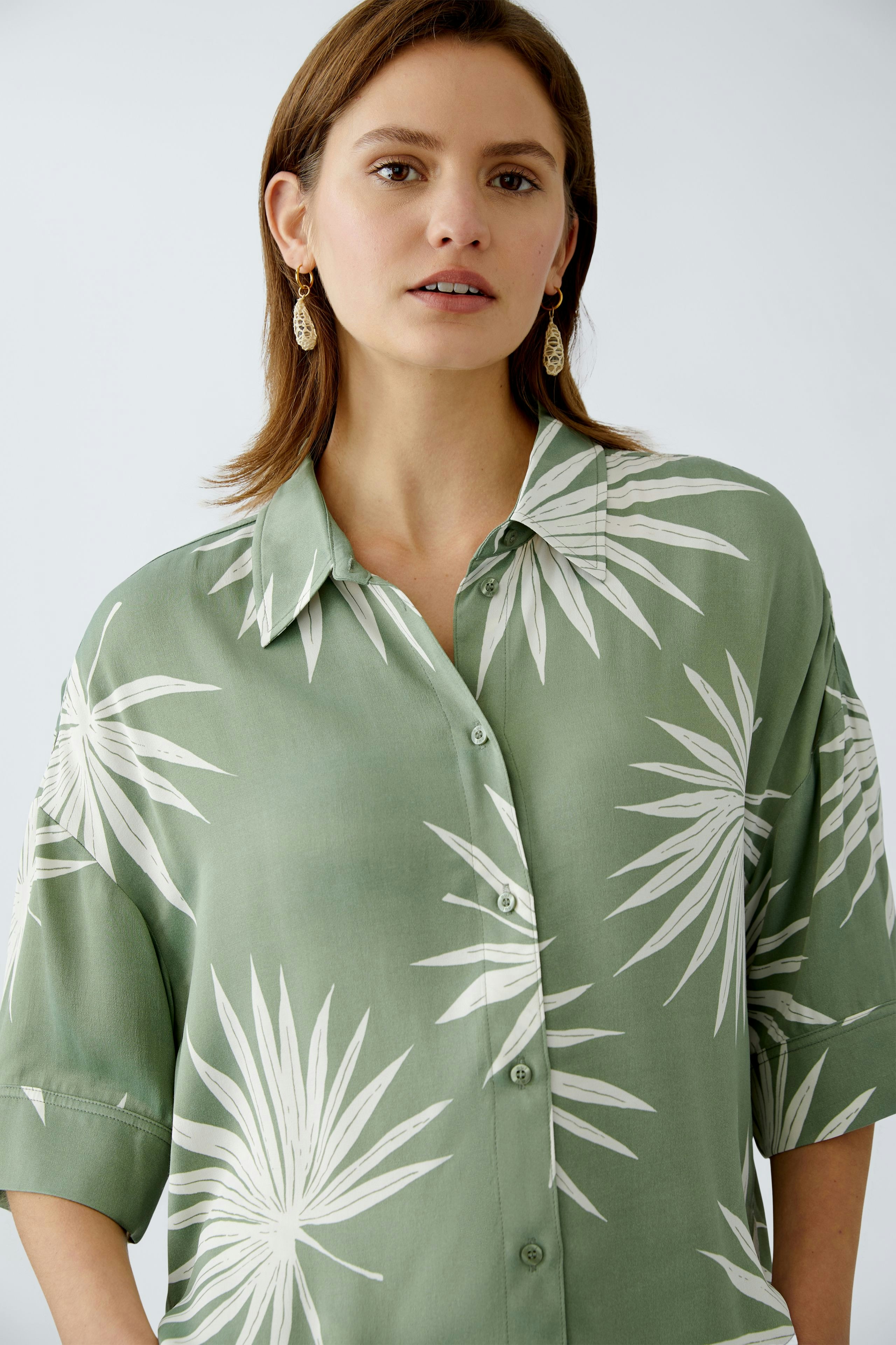 Stylish women's blouse: A woman in a green blouse with palm leaf print, exuding a fresh summer vibe.