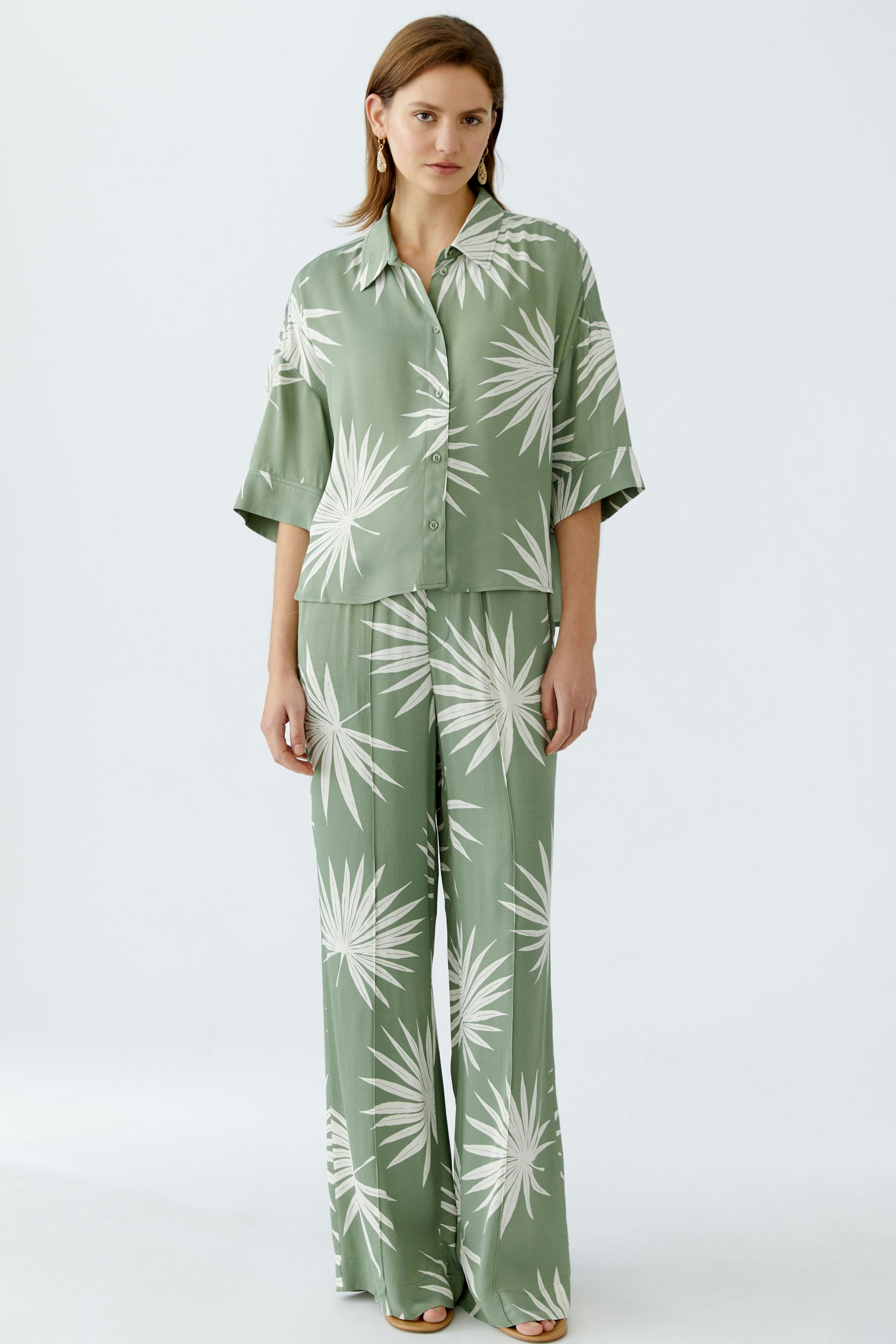 Stylish blouse: Woman in a green blouse with palm leaf print, paired with matching wide-leg pants.