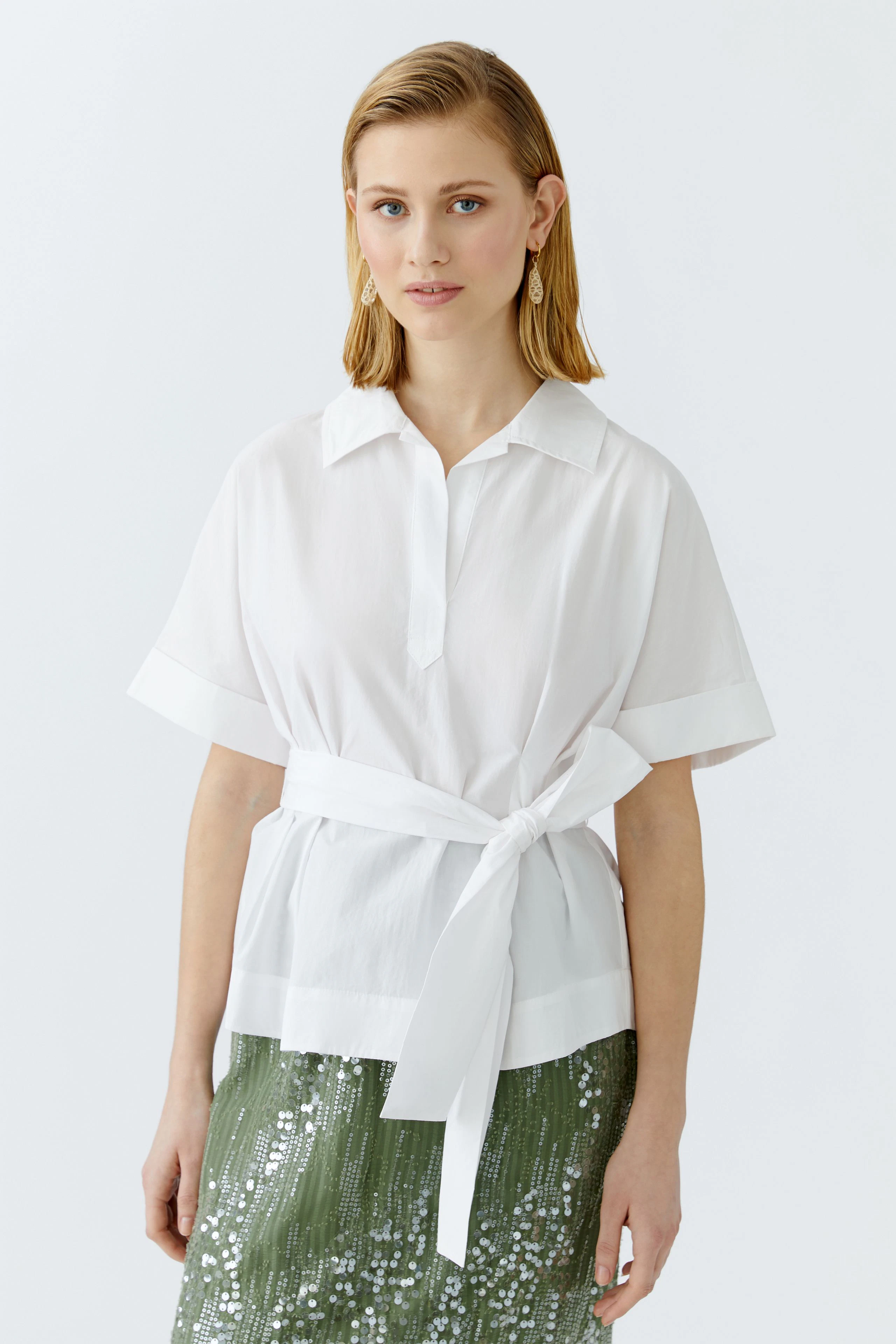 Elegante Damen-Bluse: Frau in weißer Bluse mit Gürtel und lässigem Schnitt, ideal für jeden Anlass.