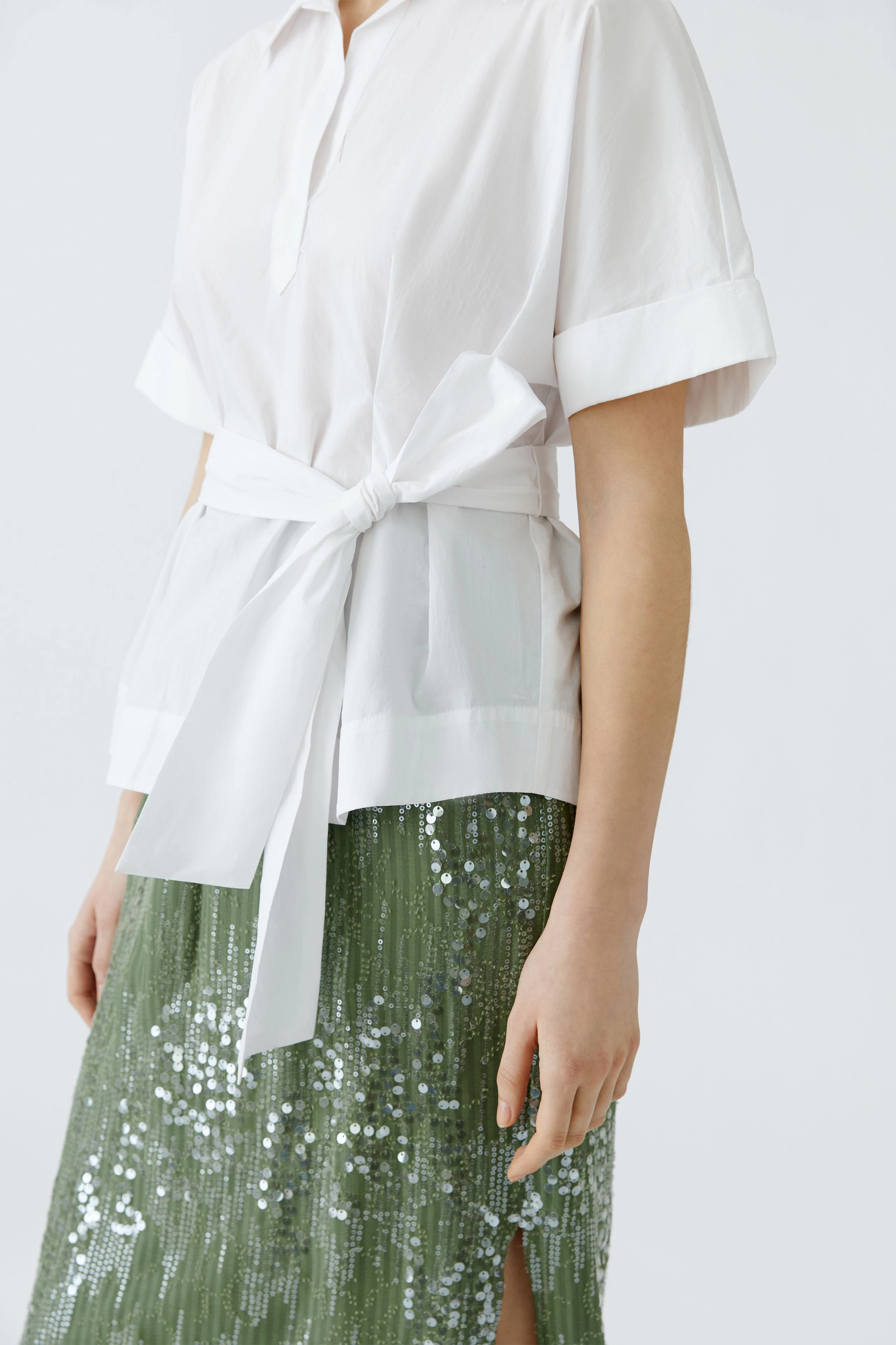 Elegante Damen-Bluse: Frau in weißer Bluse mit Taillengürtel und schimmerndem Rock.