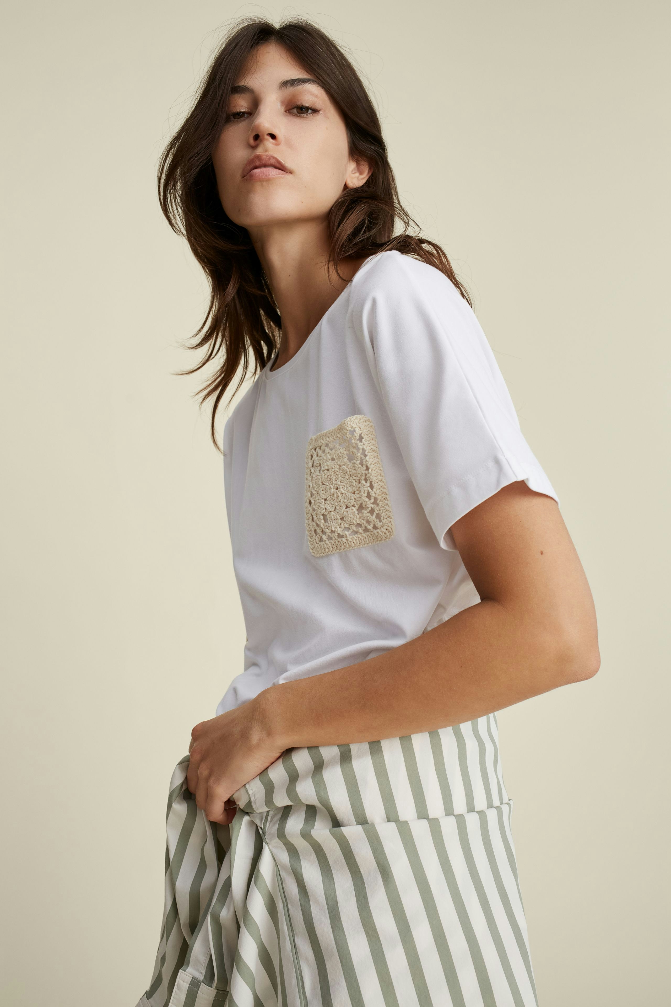 Moderne Damen-Bluse: Frau in weißer Bluse mit dekorativer Tasche, lässig und stilvoll.