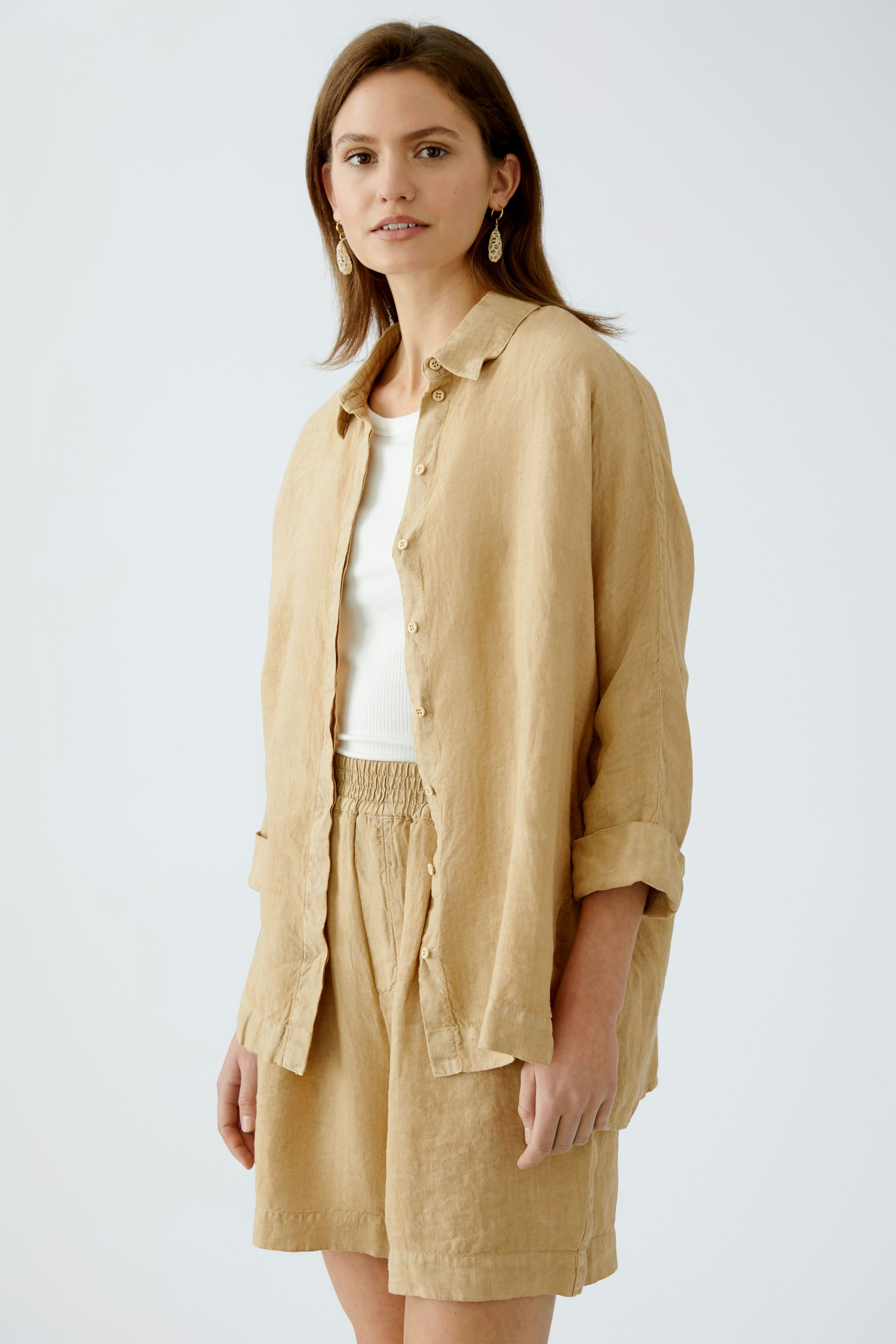 Bequeme Damen-Bluse: Junge Frau in einer leichten, beigen Bluse mit Knöpfen und lässiger Shorts.