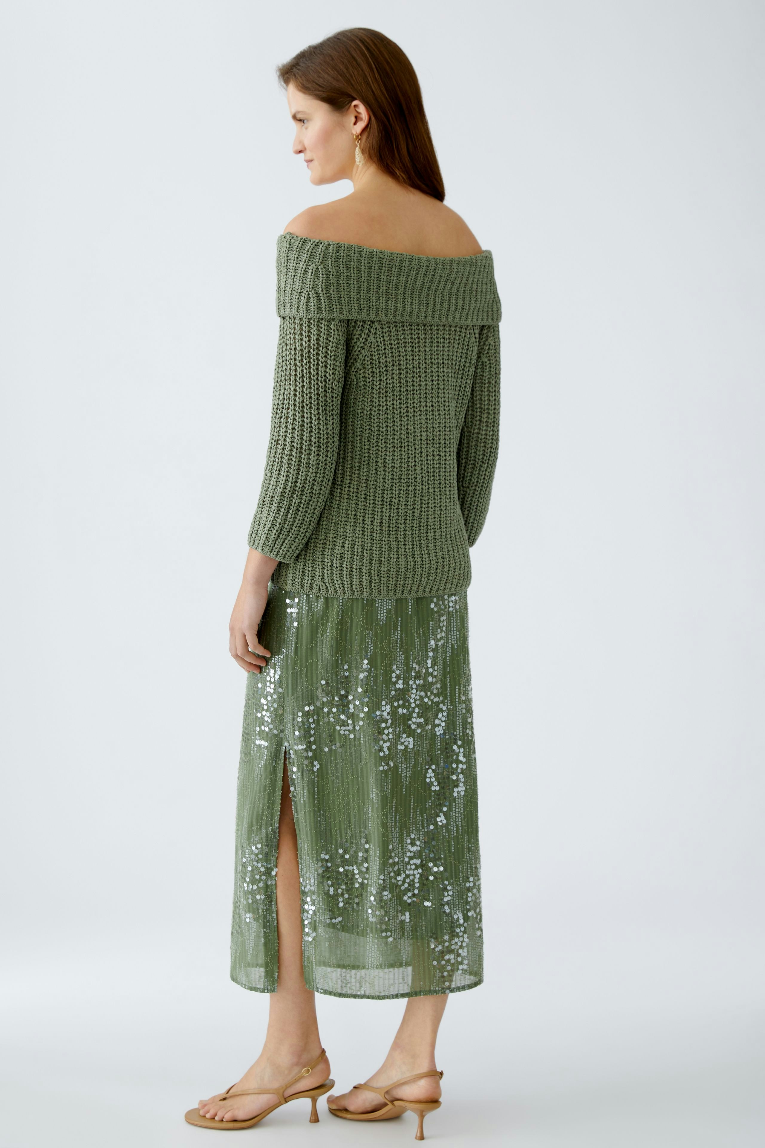 Stylish women's pullover: A woman in a green off-shoulder knitted pullover paired with a sequined skirt.