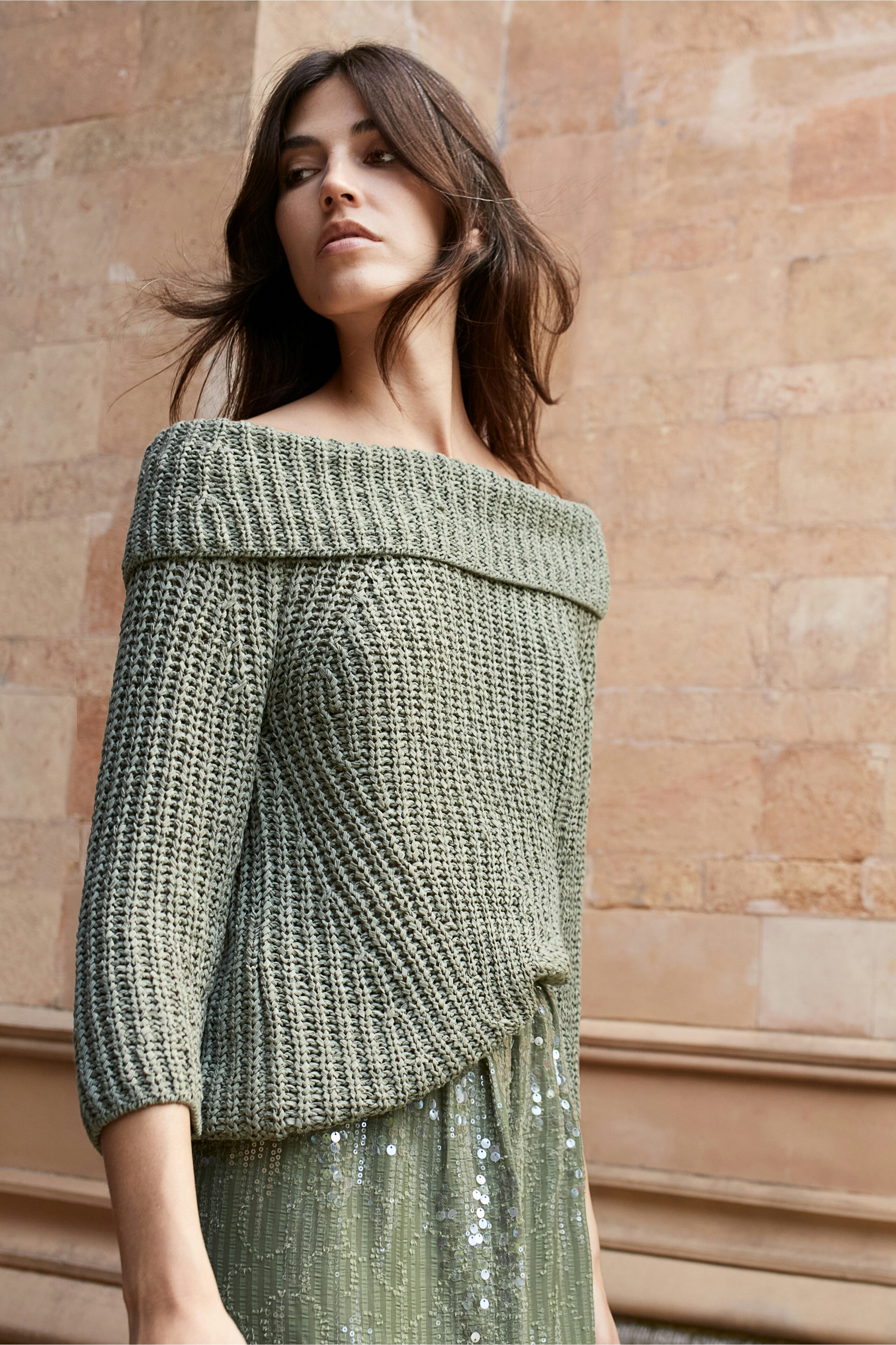 Stylish women's pullover: A woman in a green knitted pullover with an off-shoulder design.