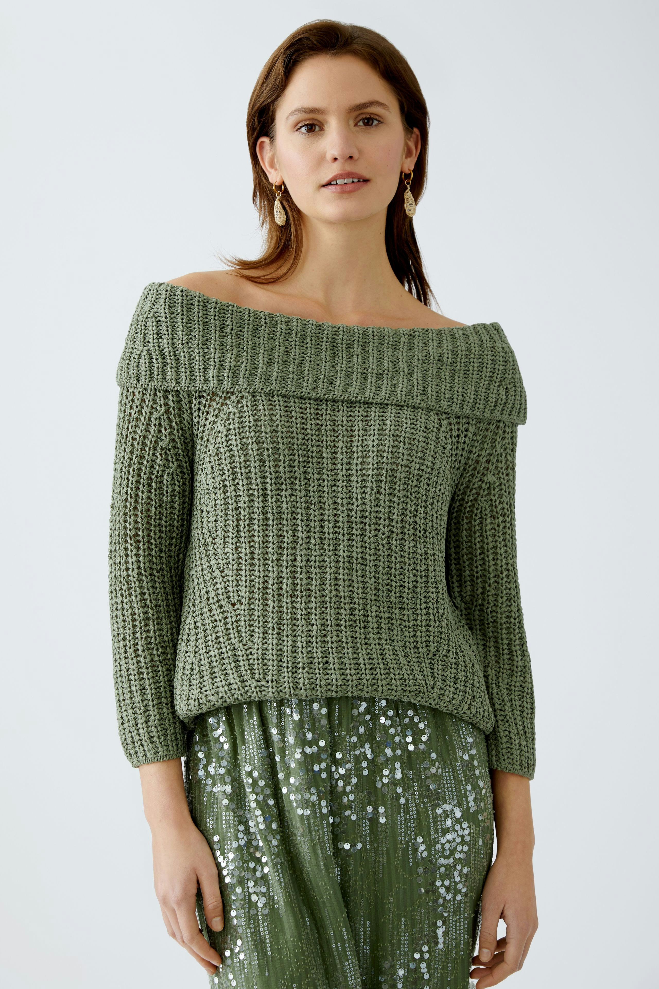 Stylish women's pullover: A woman in a green off-shoulder knitted pullover, paired with a sparkling skirt.