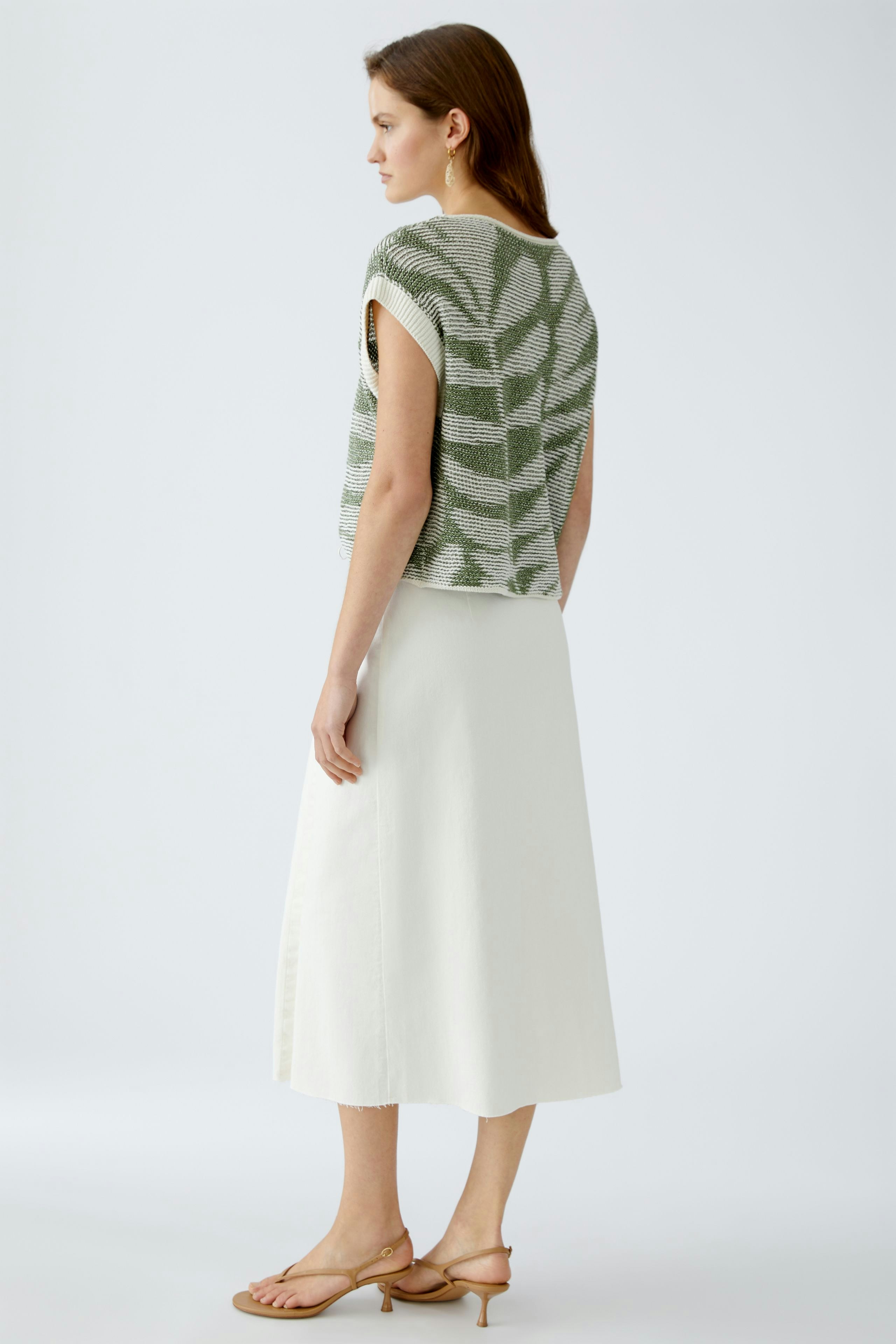 Stylish women's pullover: A woman in a green knitted pullover with a relaxed fit, paired with a white skirt.