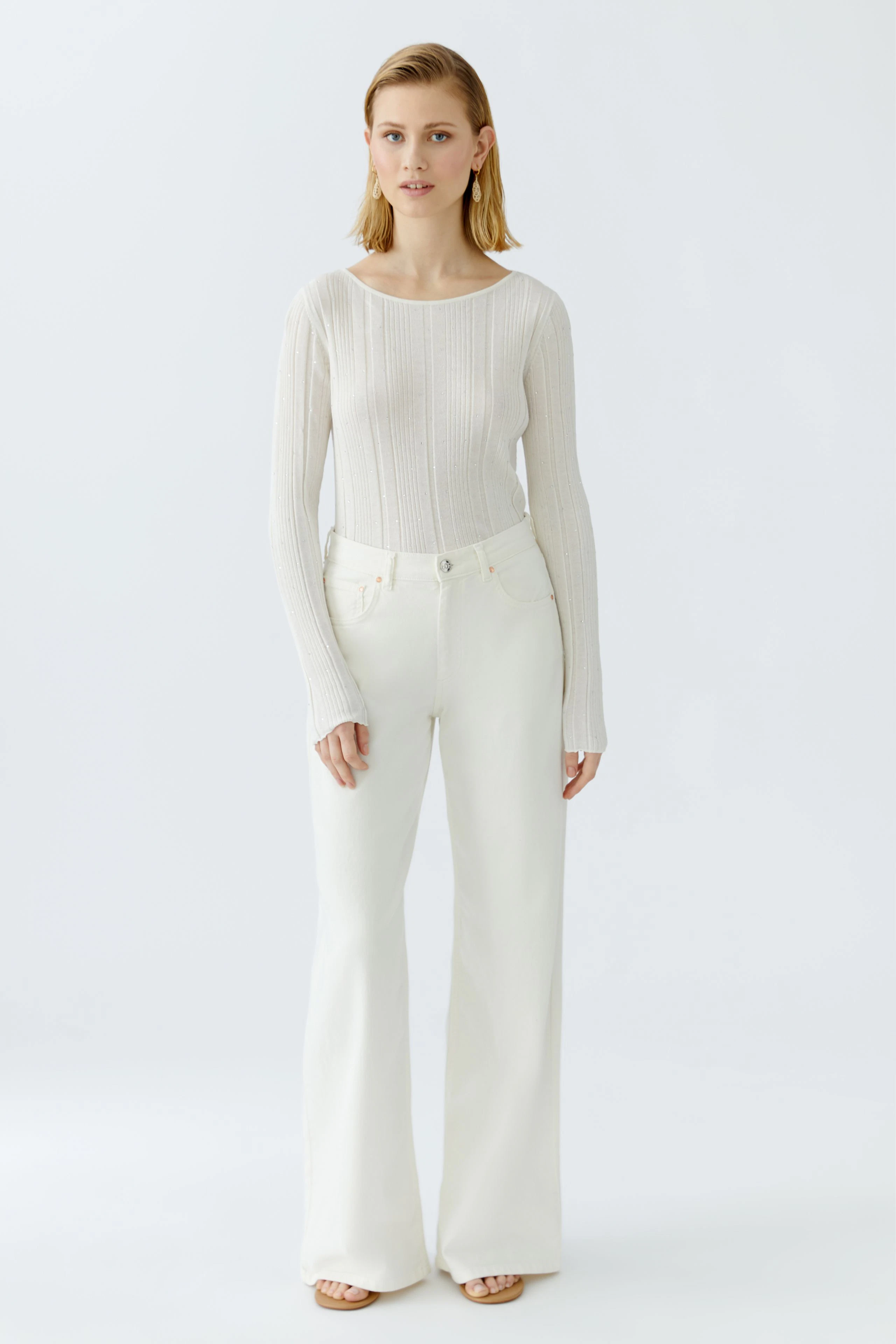 Eleganter Damen-Pullover in hellem Strick, kombiniert mit weißen, weiten Hosen.