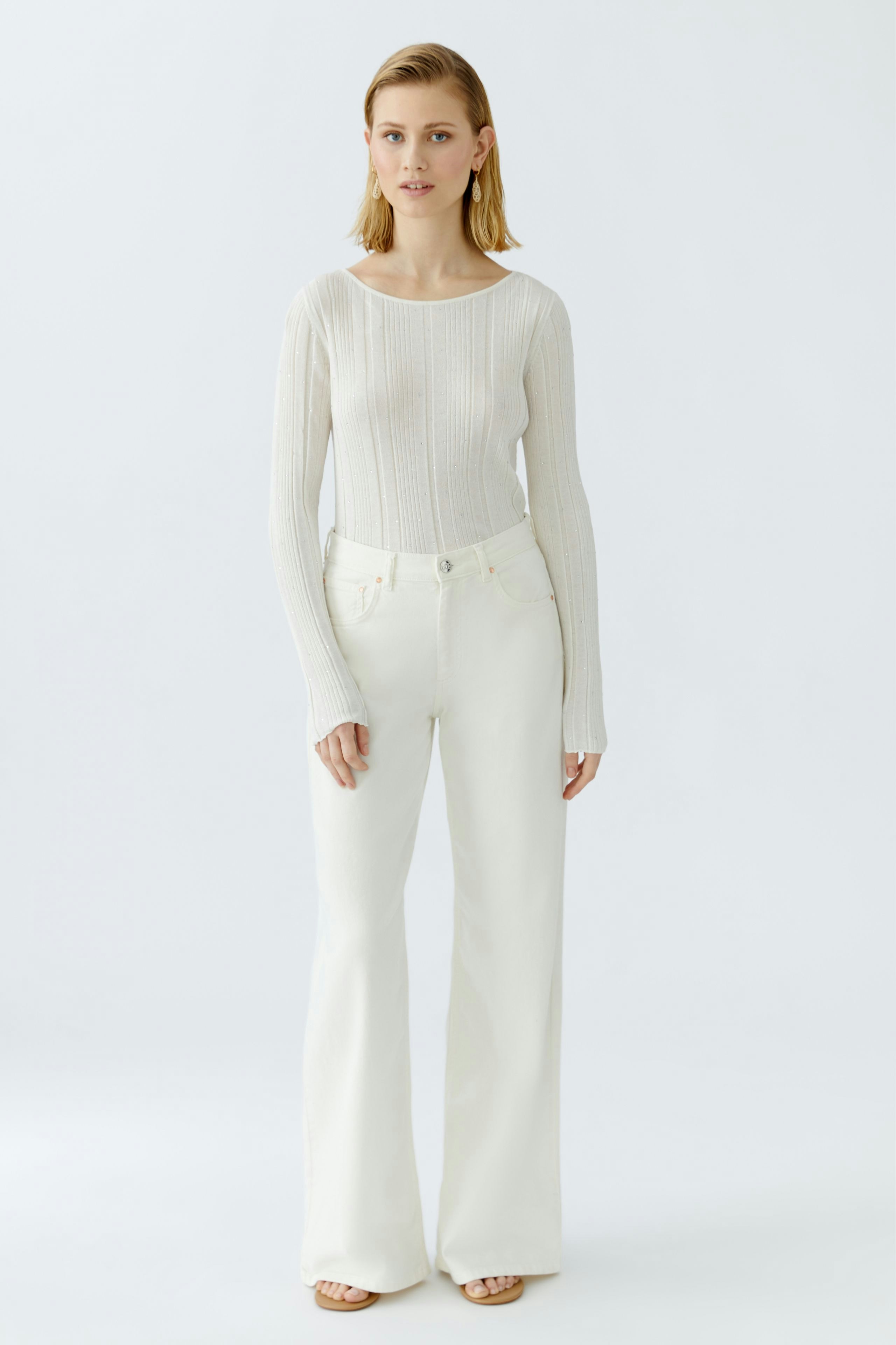 Eleganter Damen-Pullover in hellem Strick, kombiniert mit weißen, weiten Hosen.