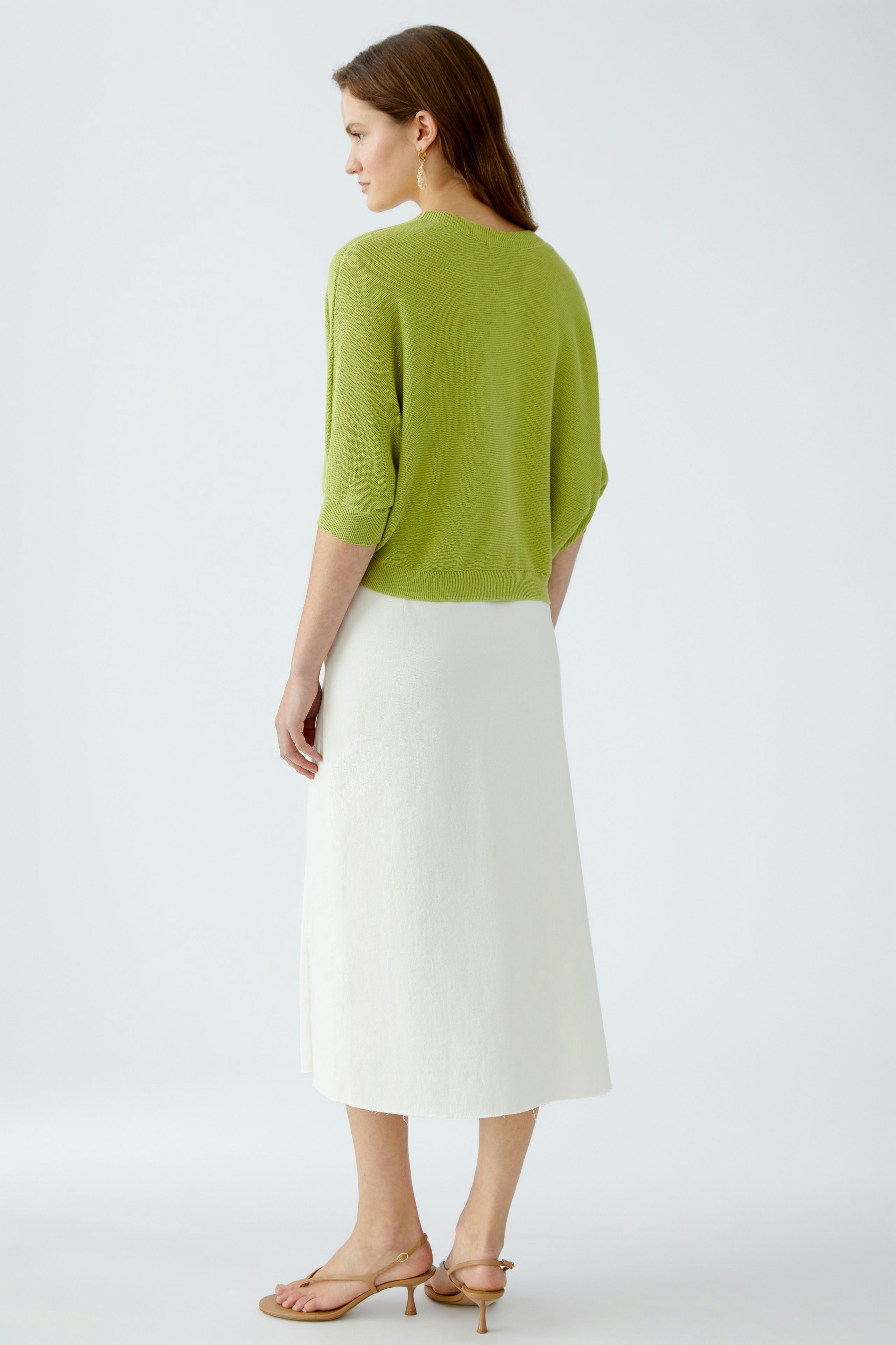 Stylish women's cardigan: A woman in a light green cardigan paired with a white skirt, showcasing a relaxed look.