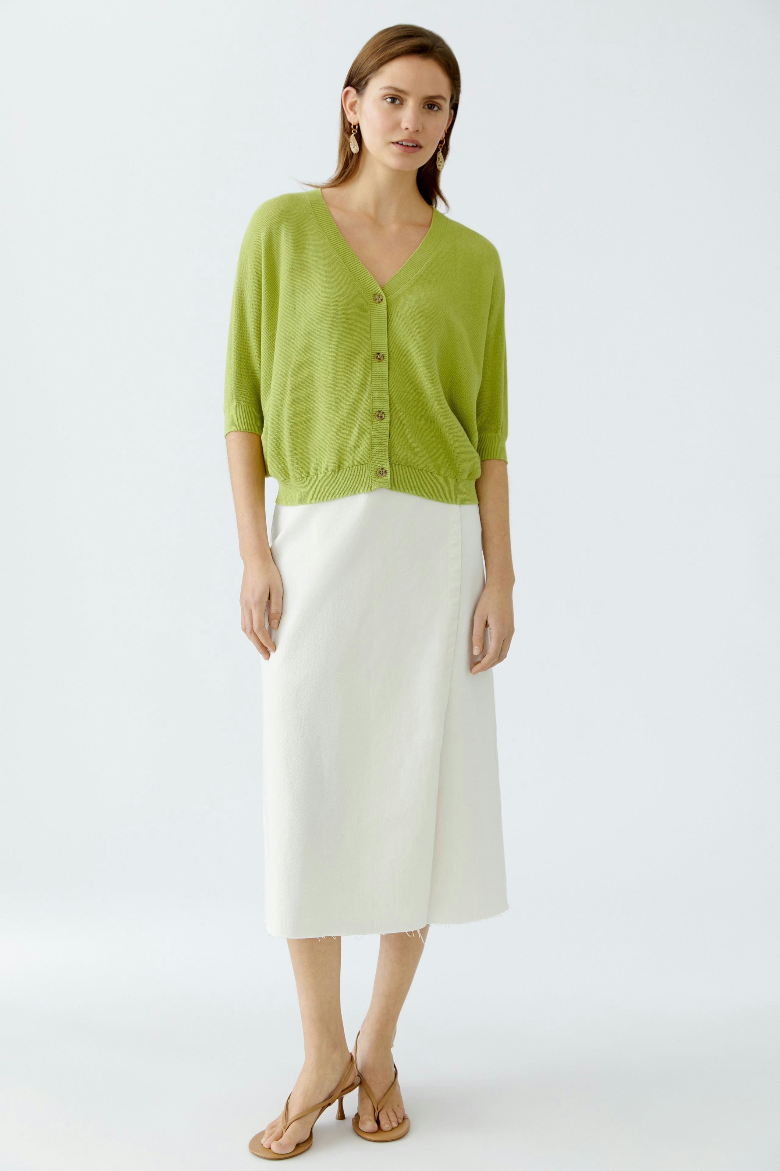 Stylish women's cardigan: A woman in a green cardigan with buttons, paired with a white skirt.