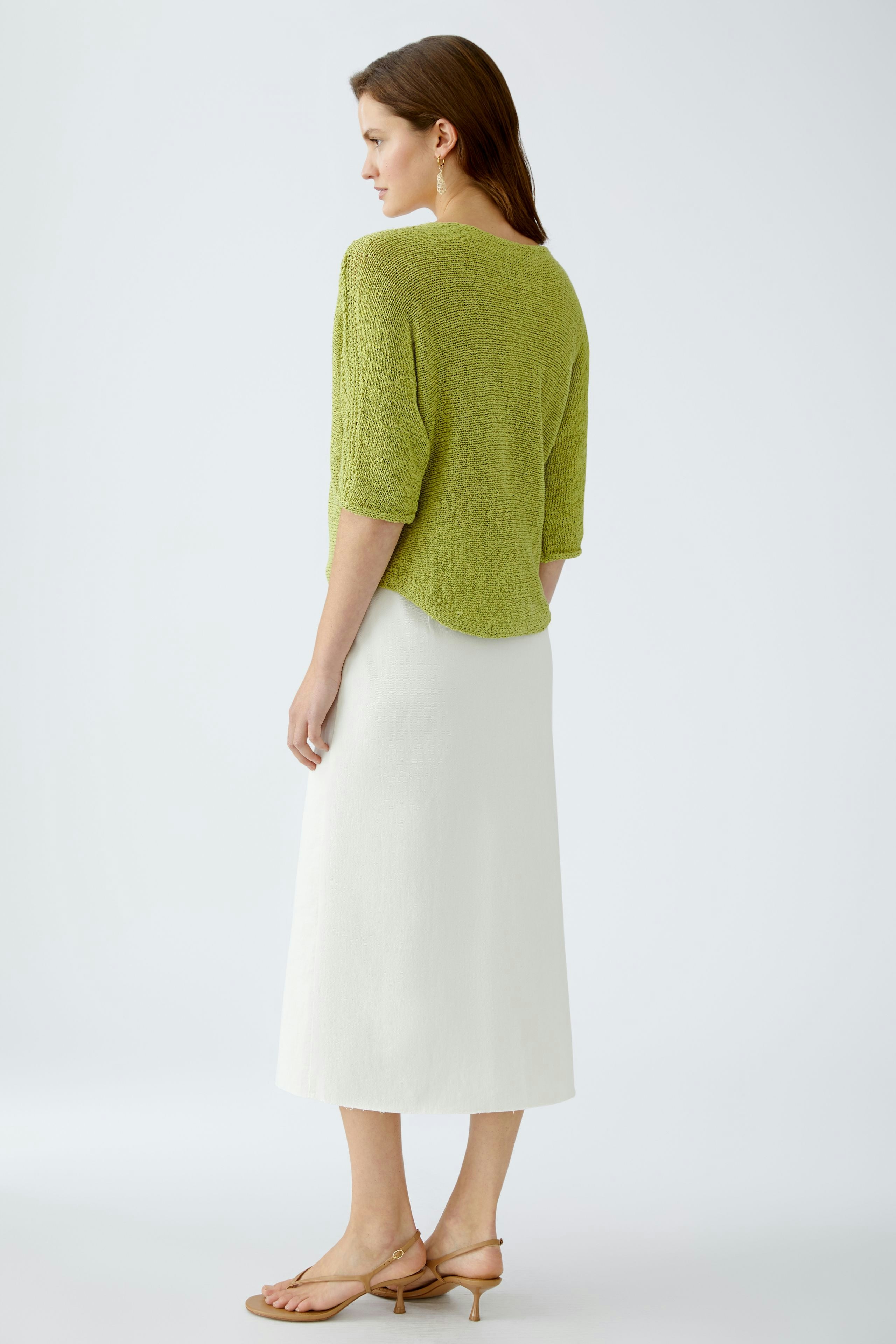 Damen-Pullover: Frau in grünem, lässigem Strickpullover mit kurzen Ärmeln und weißem Rock.