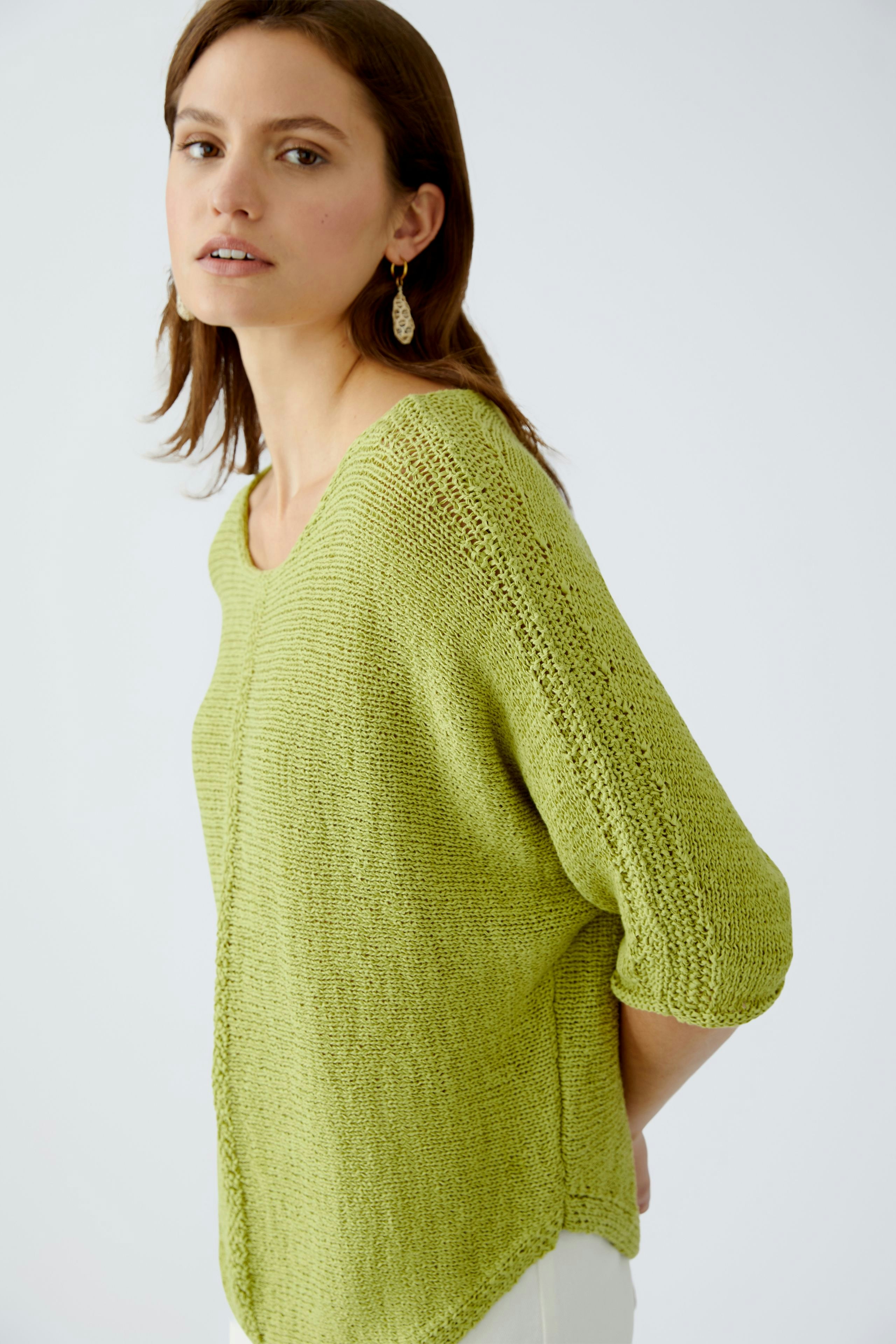 Damen-Pullover: Frau in einem leichten, grünen Strickpullover mit lockerer Passform und V-Ausschnitt.