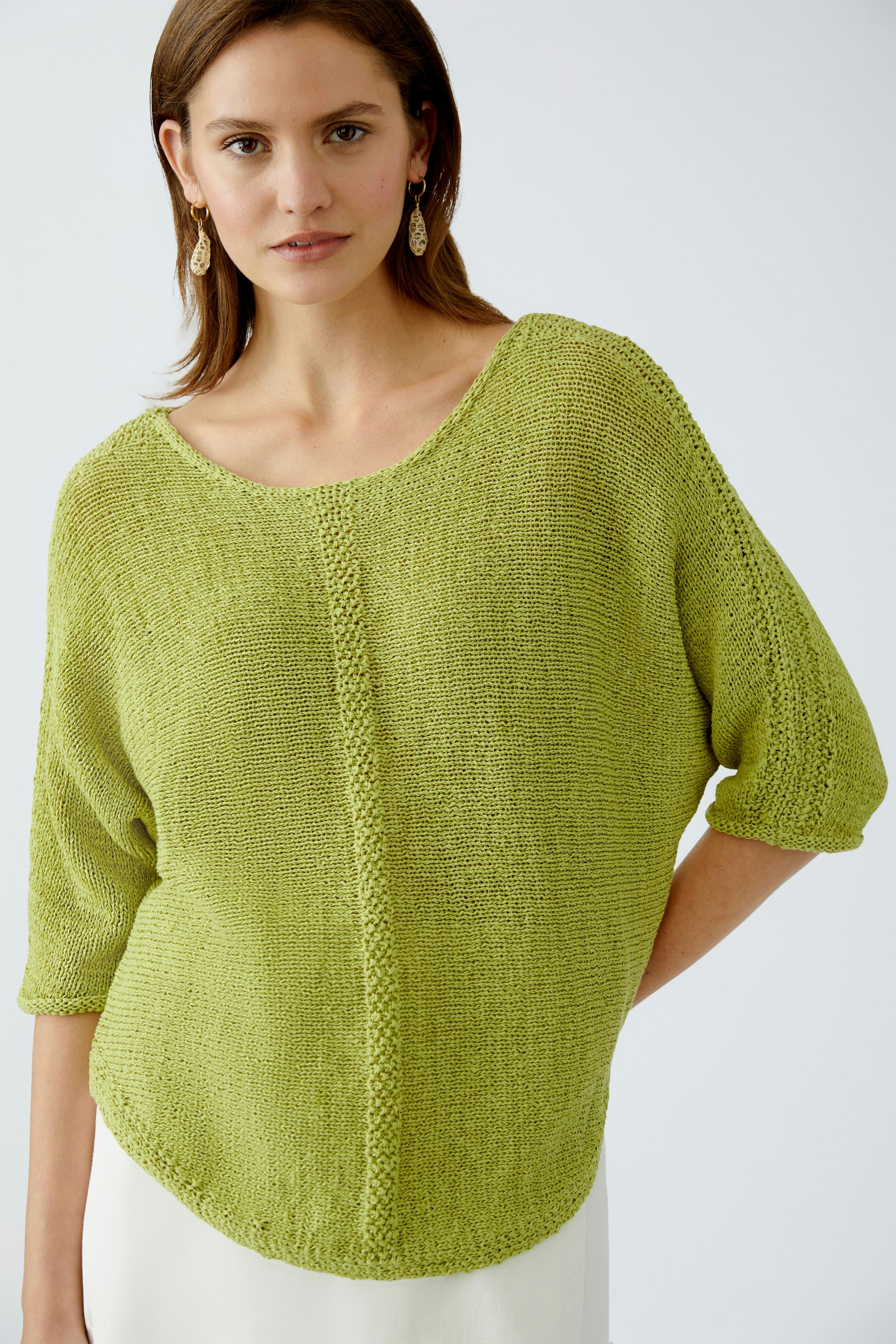 Damen-Pullover: Frau in einem leichten, grünen Strickpullover mit lässigem Schnitt und kurzen Ärmeln.