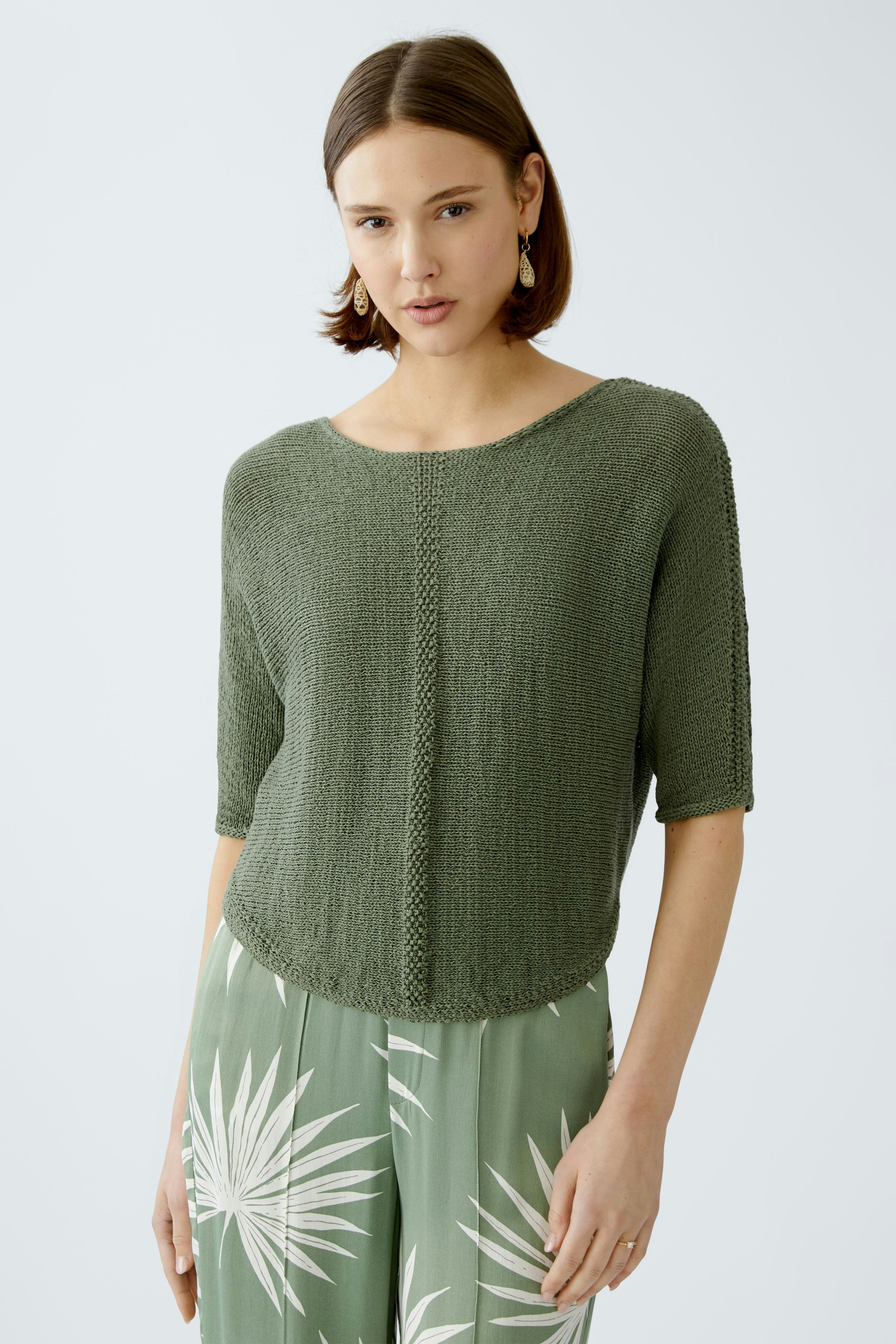 Stylish women's pullover in green, featuring a relaxed fit and short sleeves, paired with floral trousers.