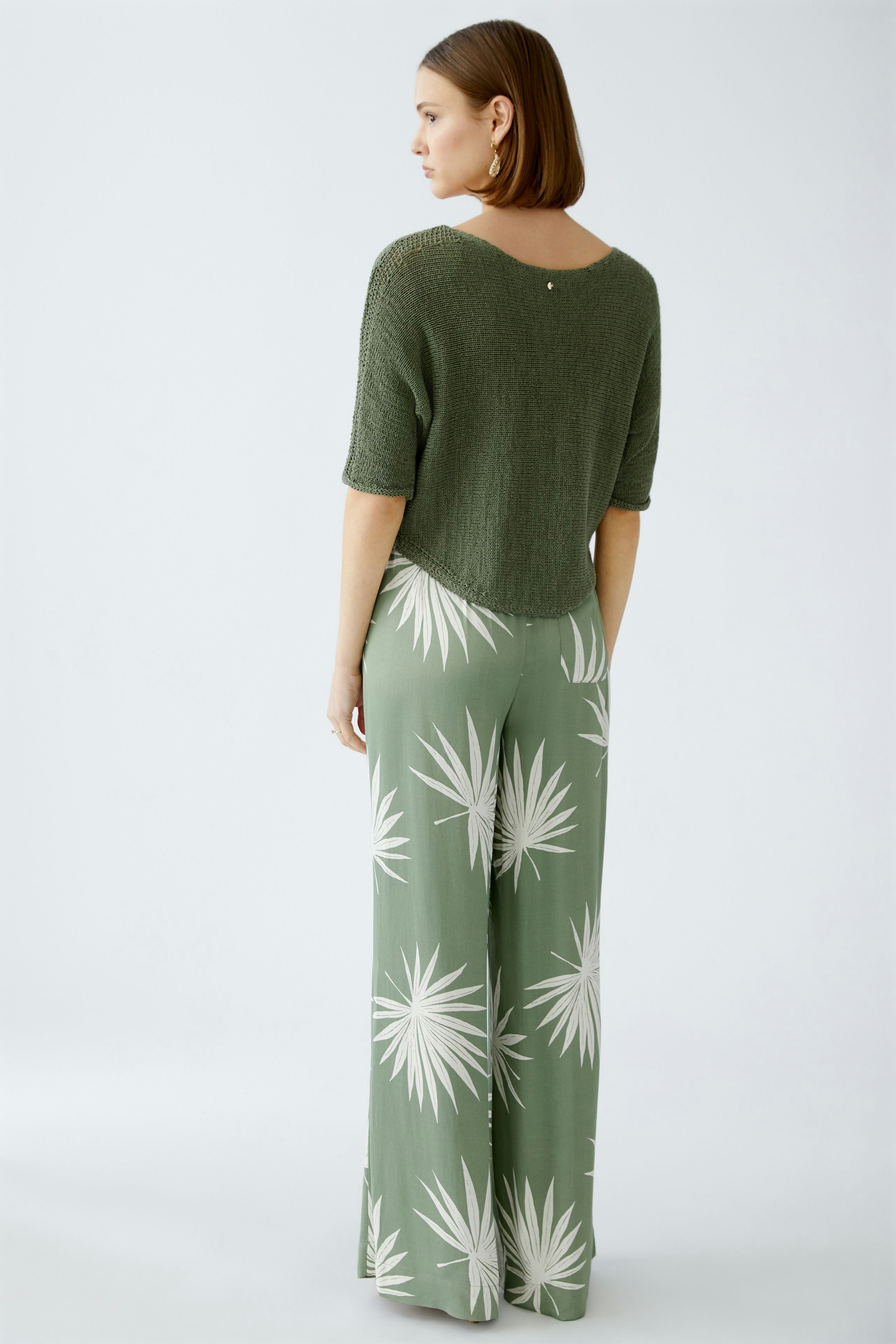 Stylish women's pullover: A woman in a green knitted pullover paired with patterned wide-leg pants.