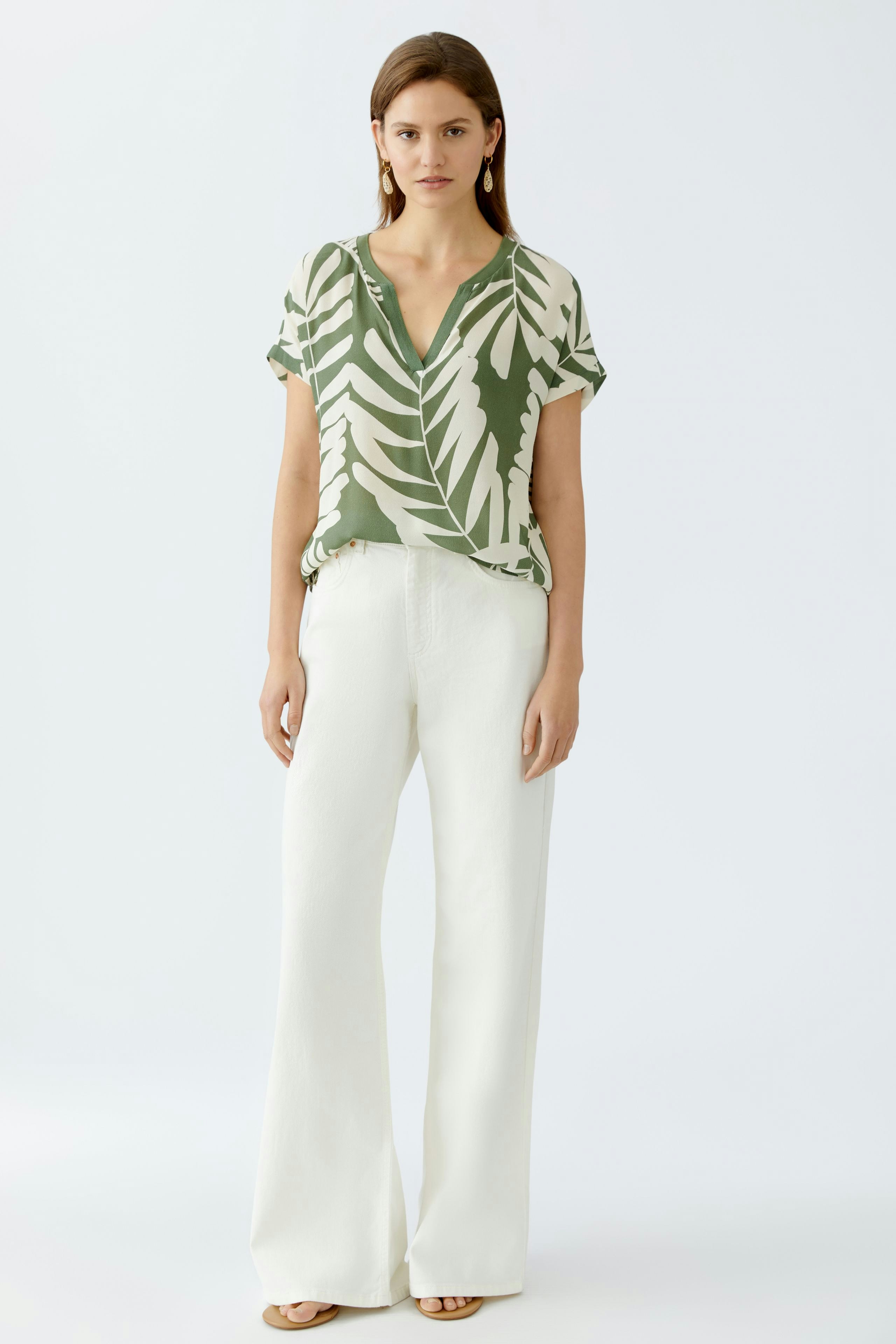 Leichtes Blusenshirt: Frau in grünem, gemustertem Shirt mit lockerer Passform und weißen Hosen.