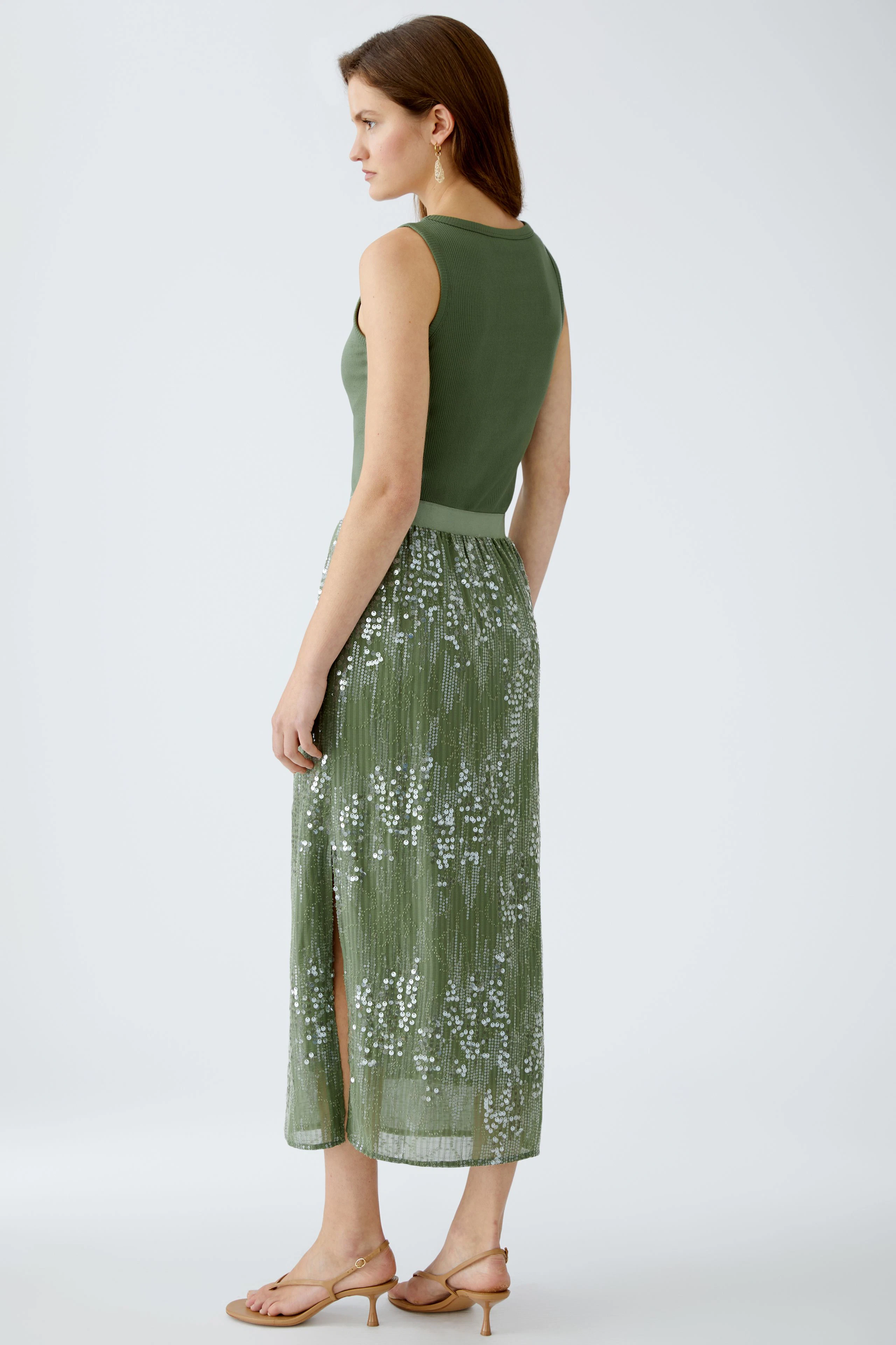 Elegant pencil skirt: Woman in a green sequined skirt with a side slit, showcasing a stylish look.