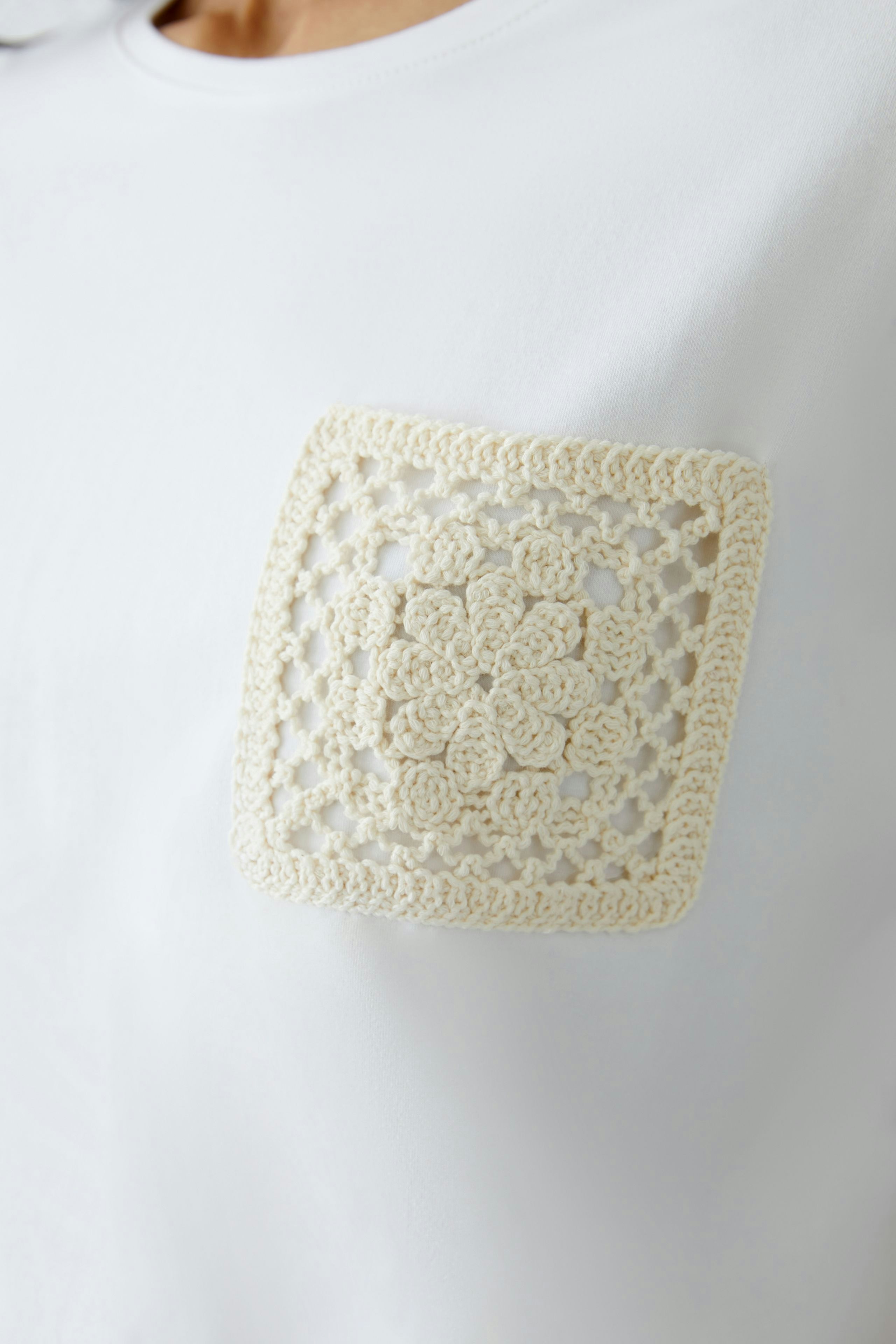 Elegantes Damen-T-Shirt in Weiß mit einem dekorativen Häkelmotiv auf der Brust.