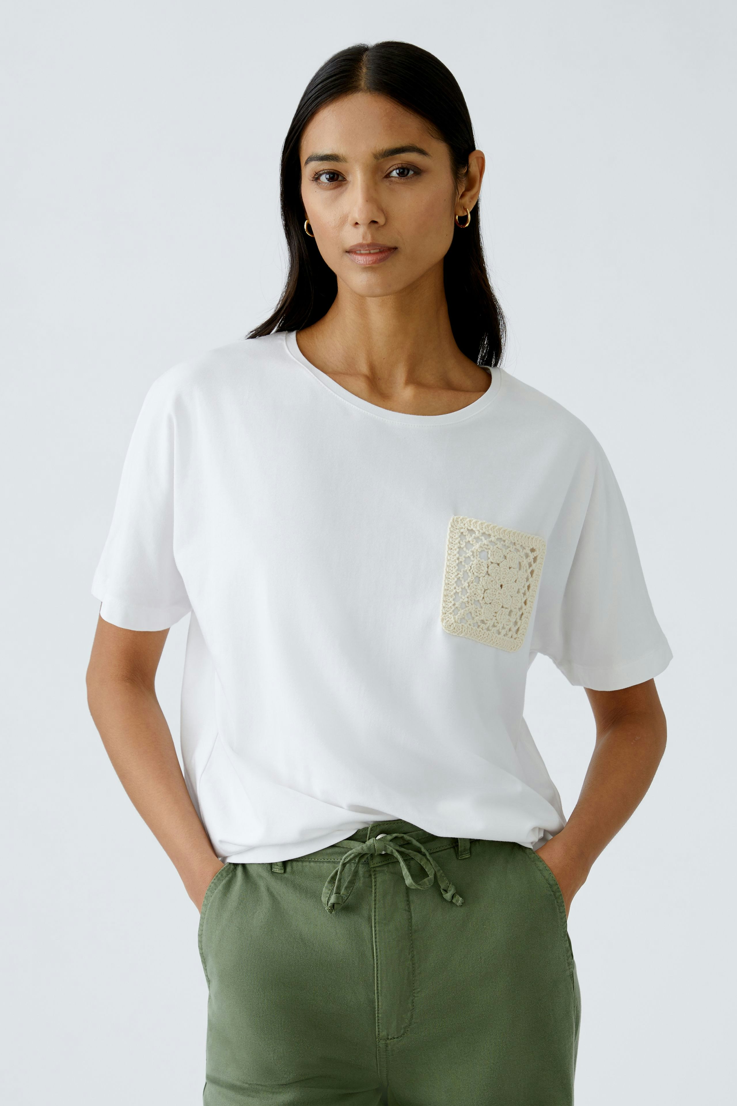Elegantes Damen-T-Shirt: Frau in weißem Shirt mit gehäkelter Tasche und lässigen Hosen.