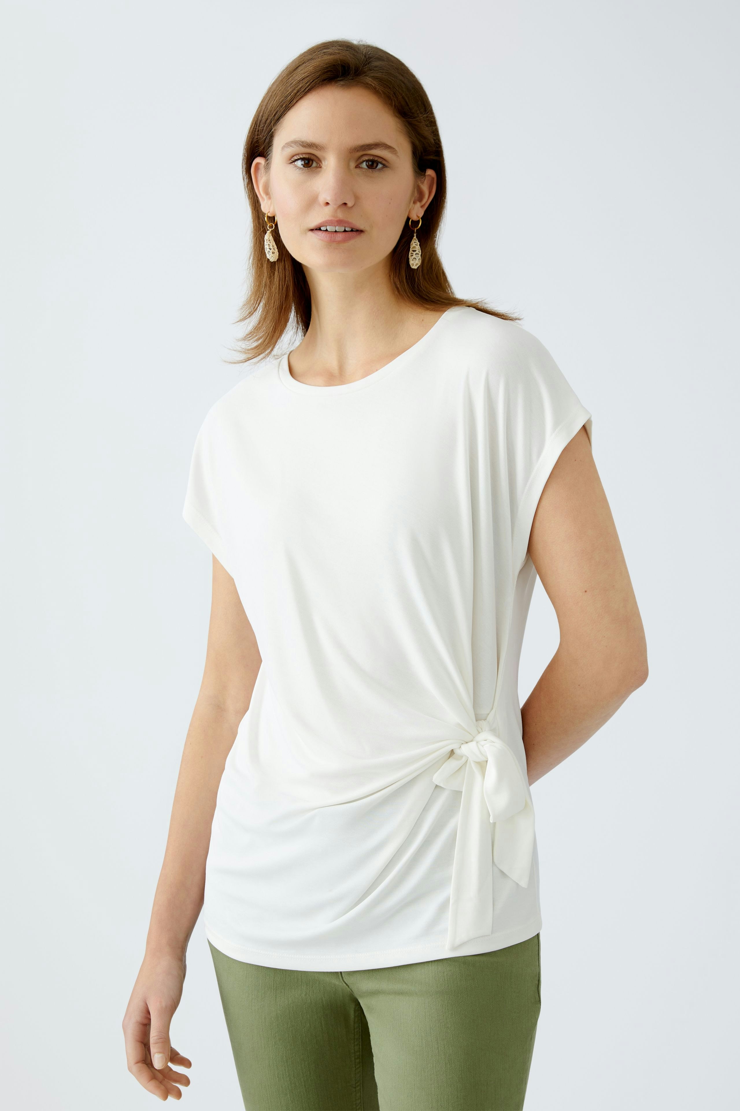 Elegantes Damen-T-Shirt: Frau in weißem T-Shirt mit seitlichem Knoten und lässiger Ausstrahlung.