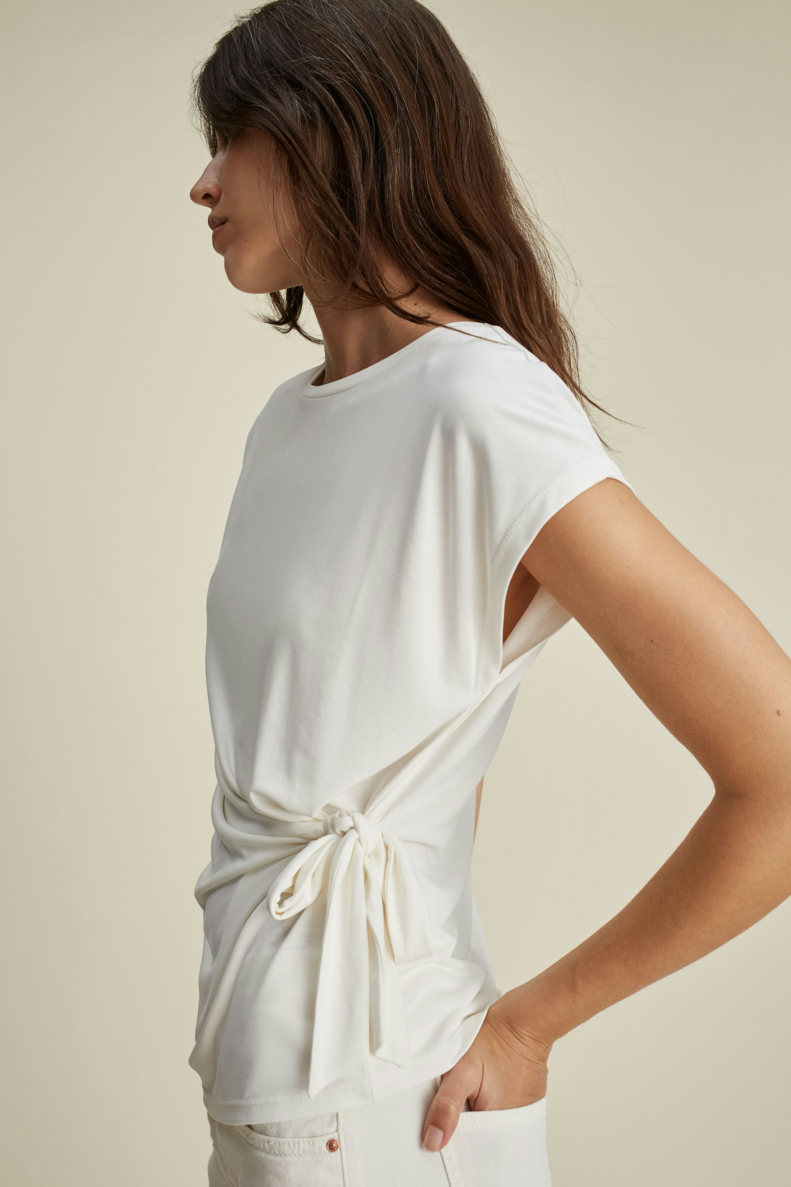 Elegantes Damen-T-Shirt: Frau in weißem T-Shirt mit seitlichem Knoten, lässiger Look.