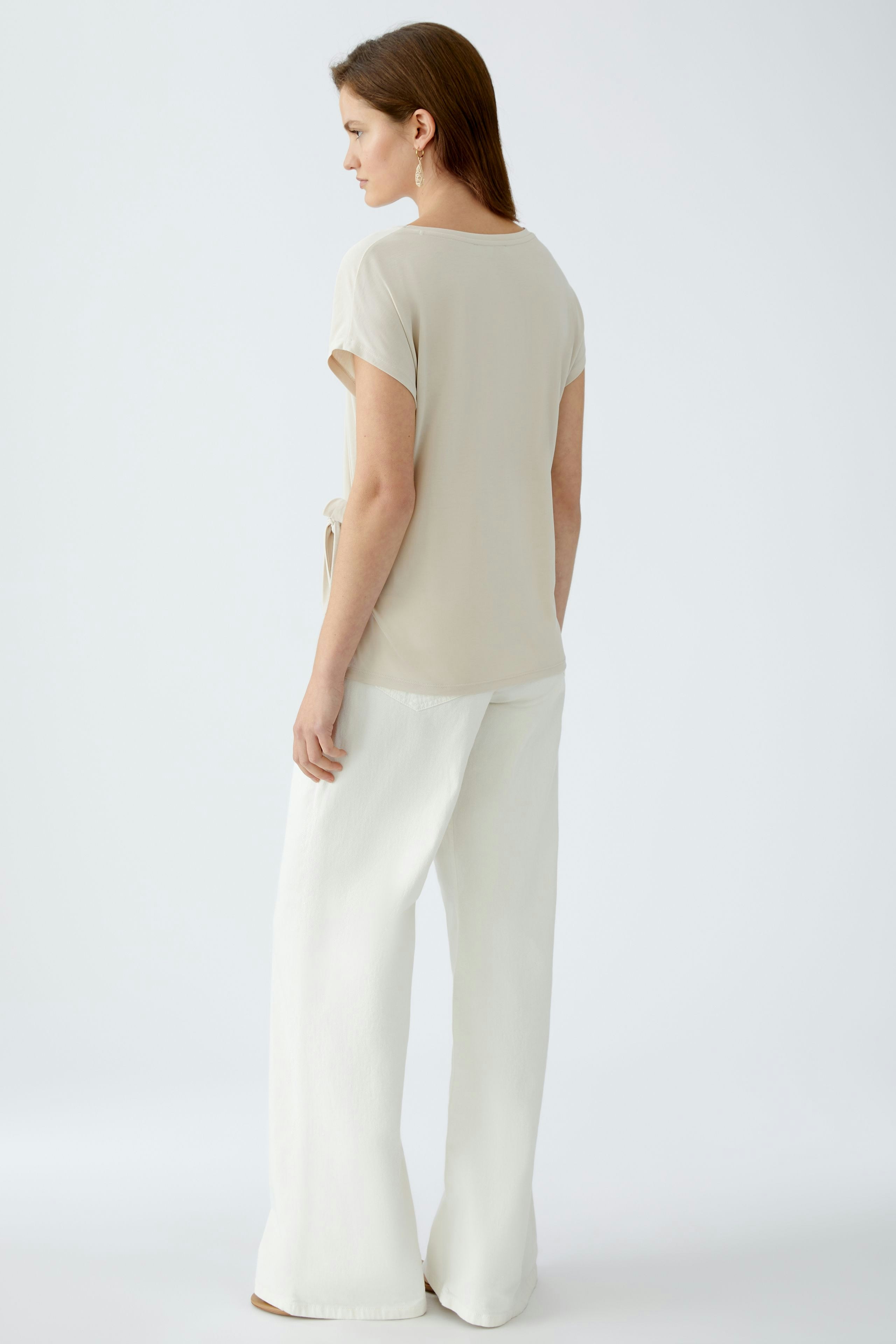Elegantes Damen-T-Shirt: Frau in beigem T-Shirt mit lässigem Schnitt und weißen, weiten Hosen.