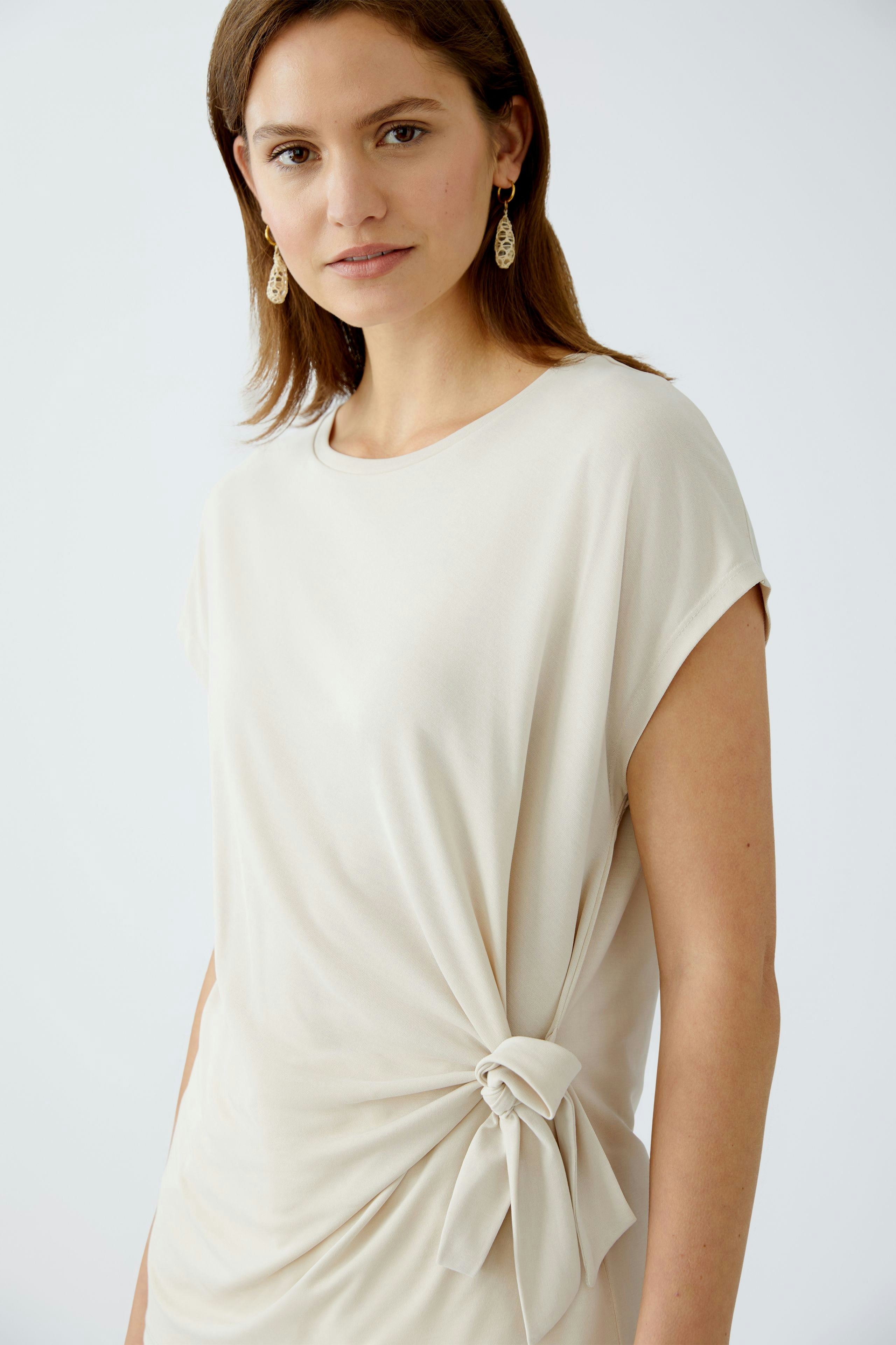 Elegantes Damen-T-Shirt: Frau in beigem T-Shirt mit Knoten-Detail, lässig und stilvoll.