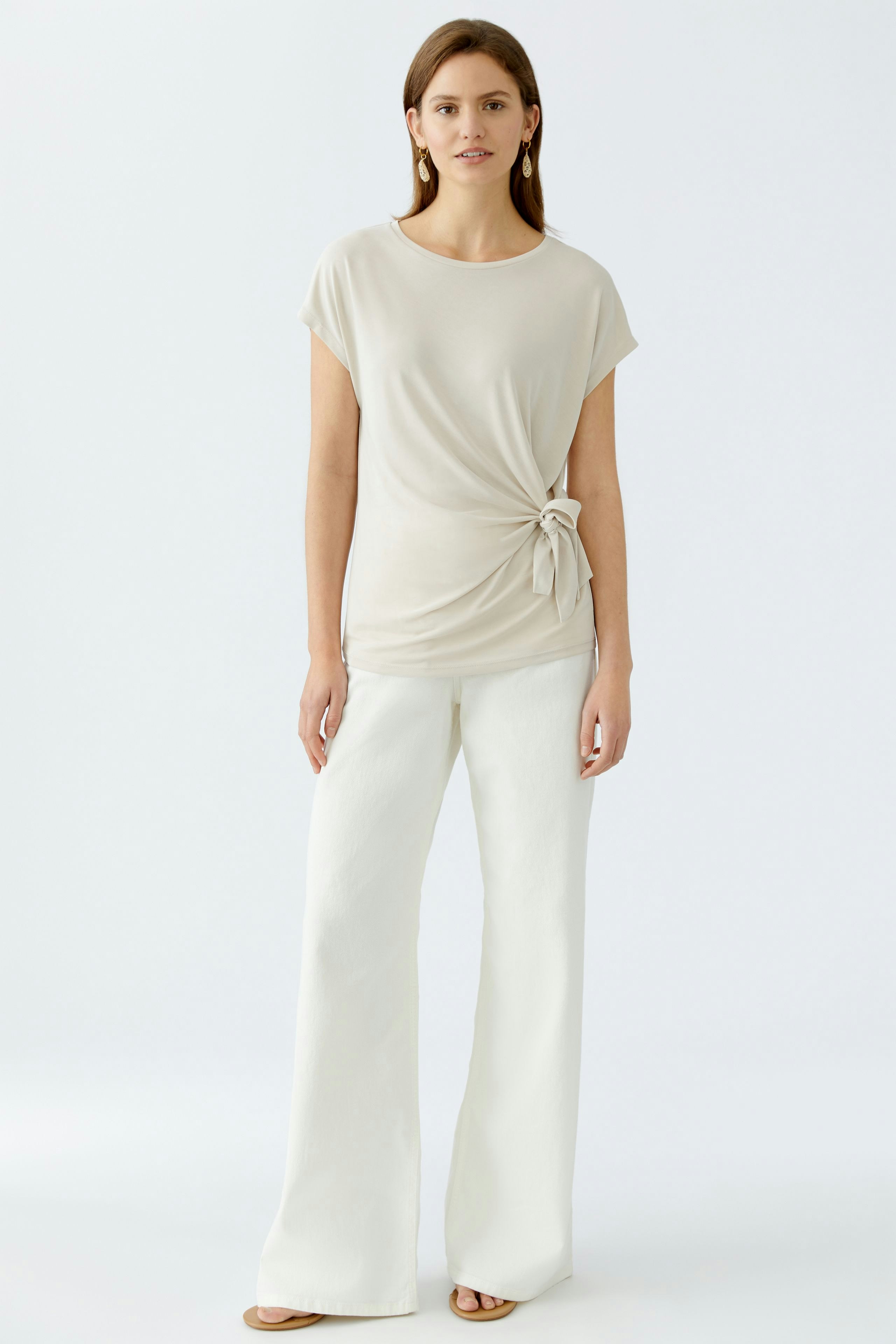 Beige Damen-T-Shirt mit lässigem Knoten-Detail, kombiniert mit weißen, weiten Hosen.