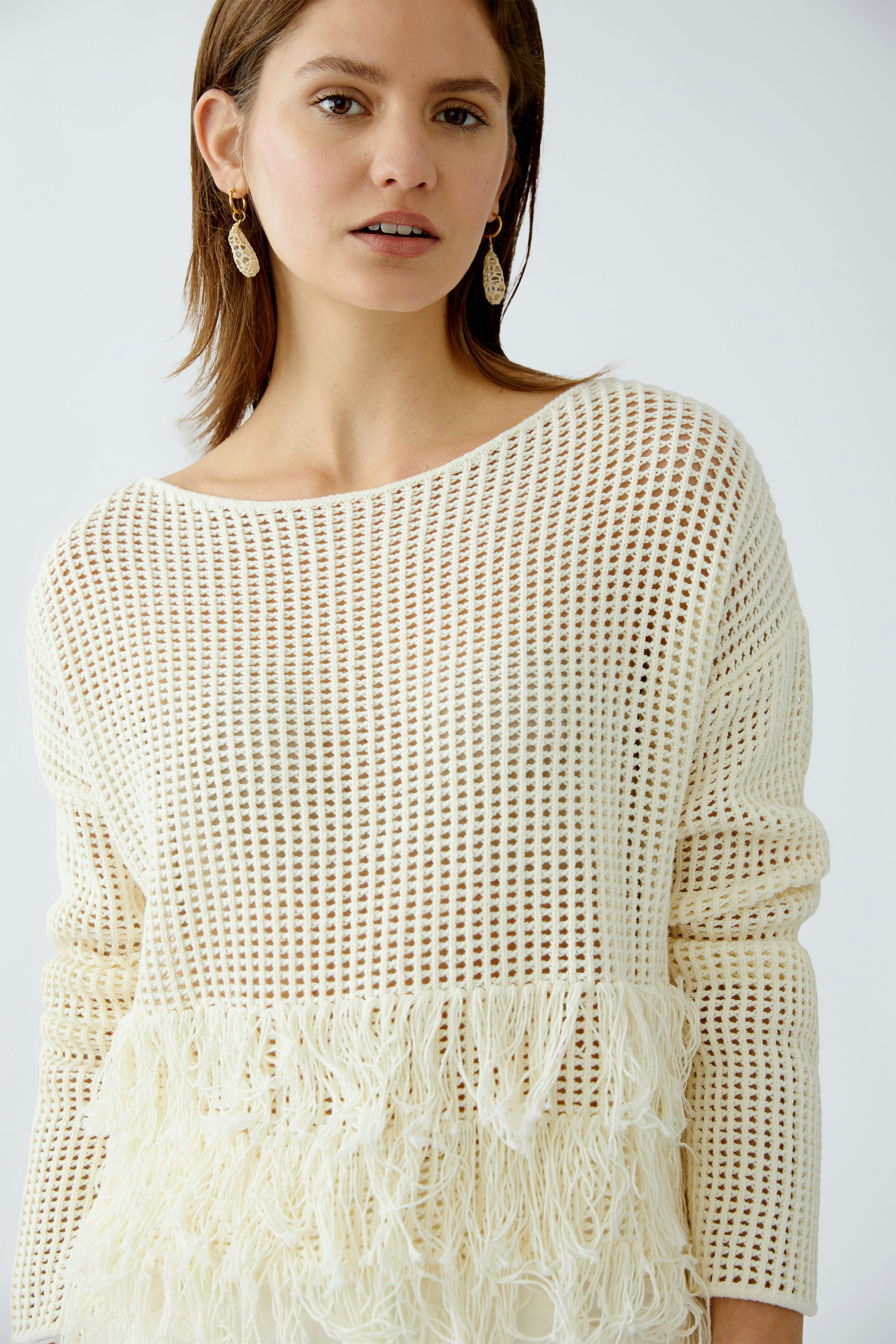Damen-Pullover: Frau in cremefarbenem, luftigen Strickpullover mit fransigem Saum.