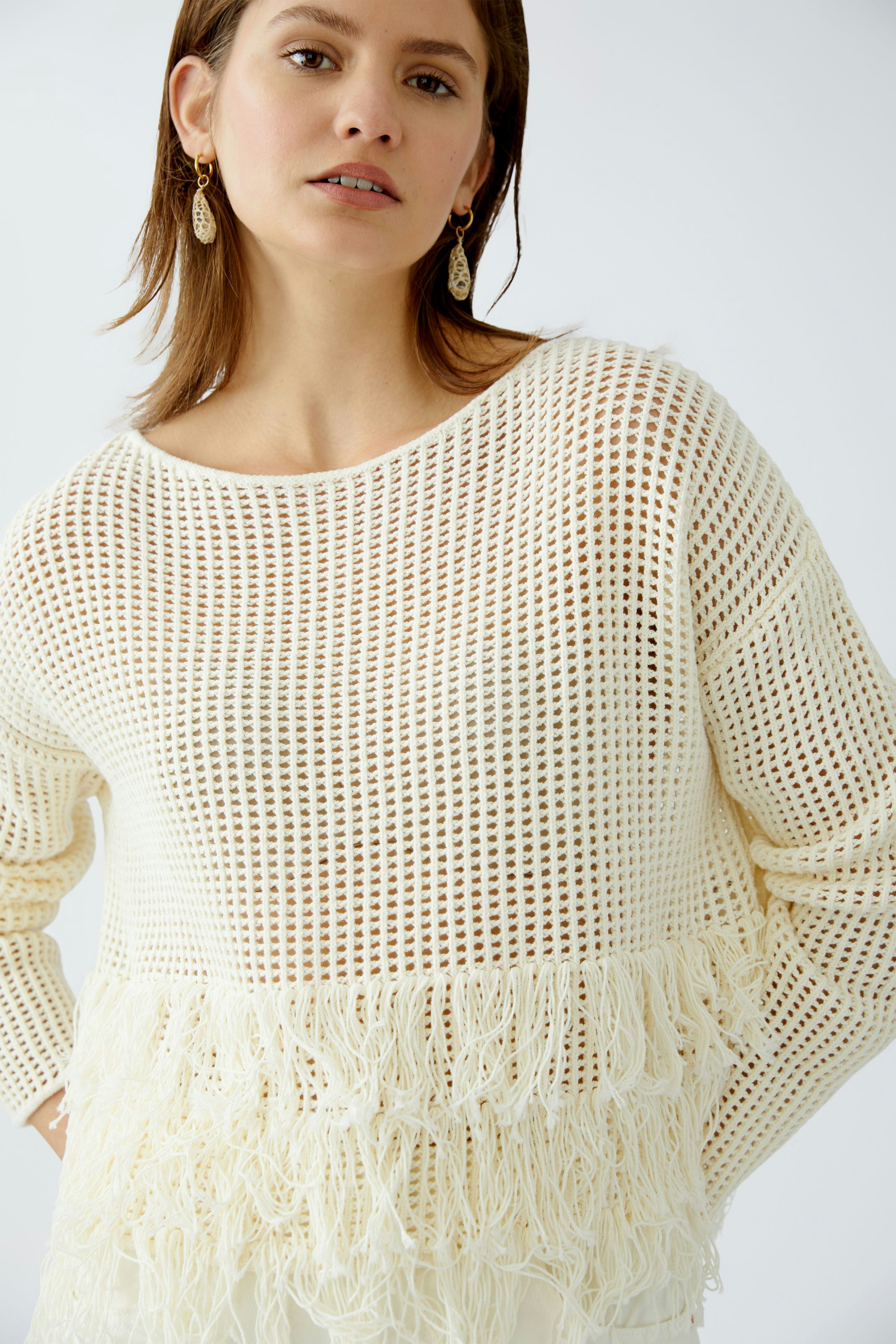 Damen-Pullover: Junge Frau in einem weißen, luftigen Strickpullover mit Fransen und lässigem Schnitt.