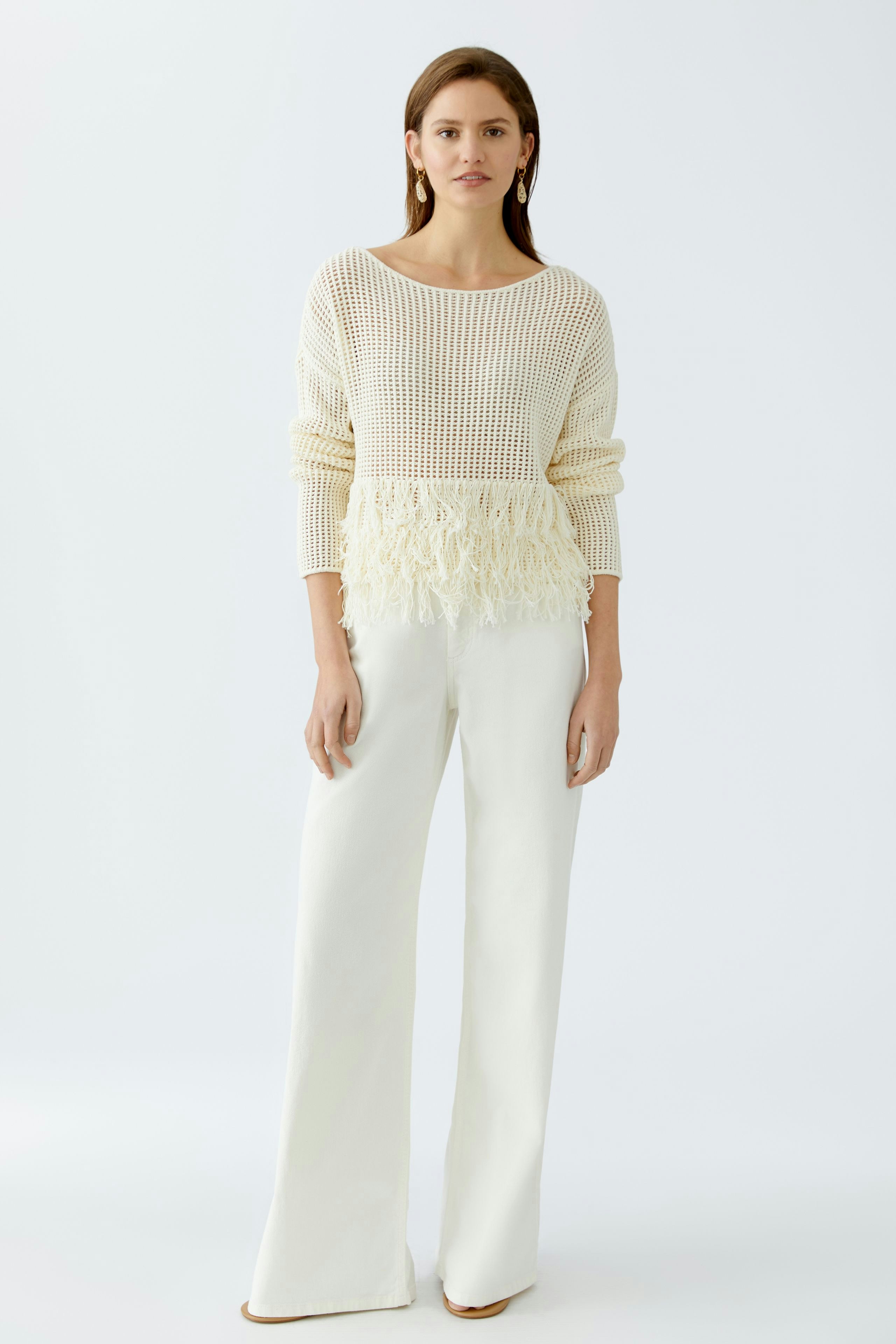 Damen-Pullover: Junge Frau in einem cremefarbenen, luftigen Strickpullover mit Fransen.