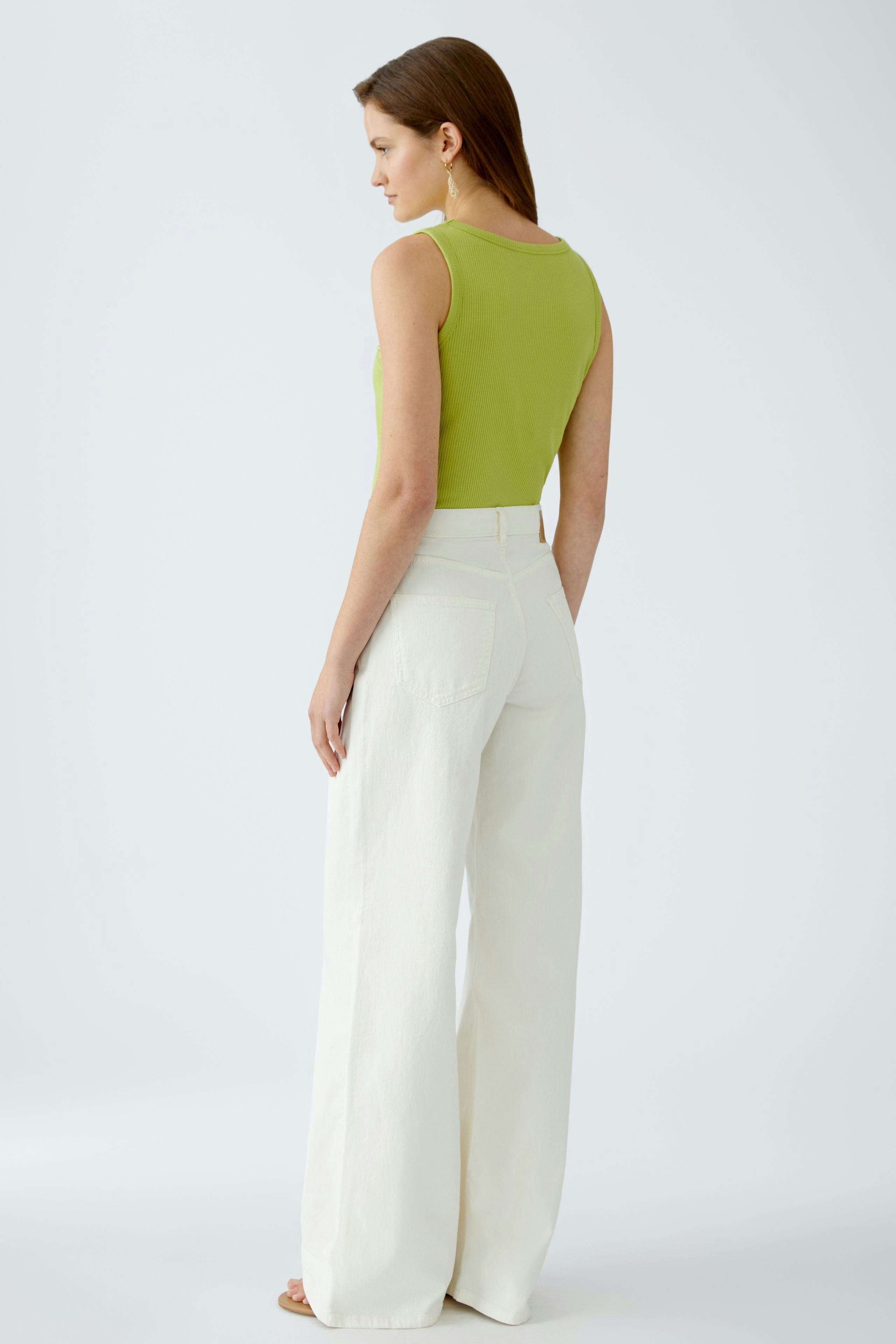 Damen Jeans Flared: Frau in weißen, weiten Jeans mit lässigem Schnitt und grünem Top von hinten.