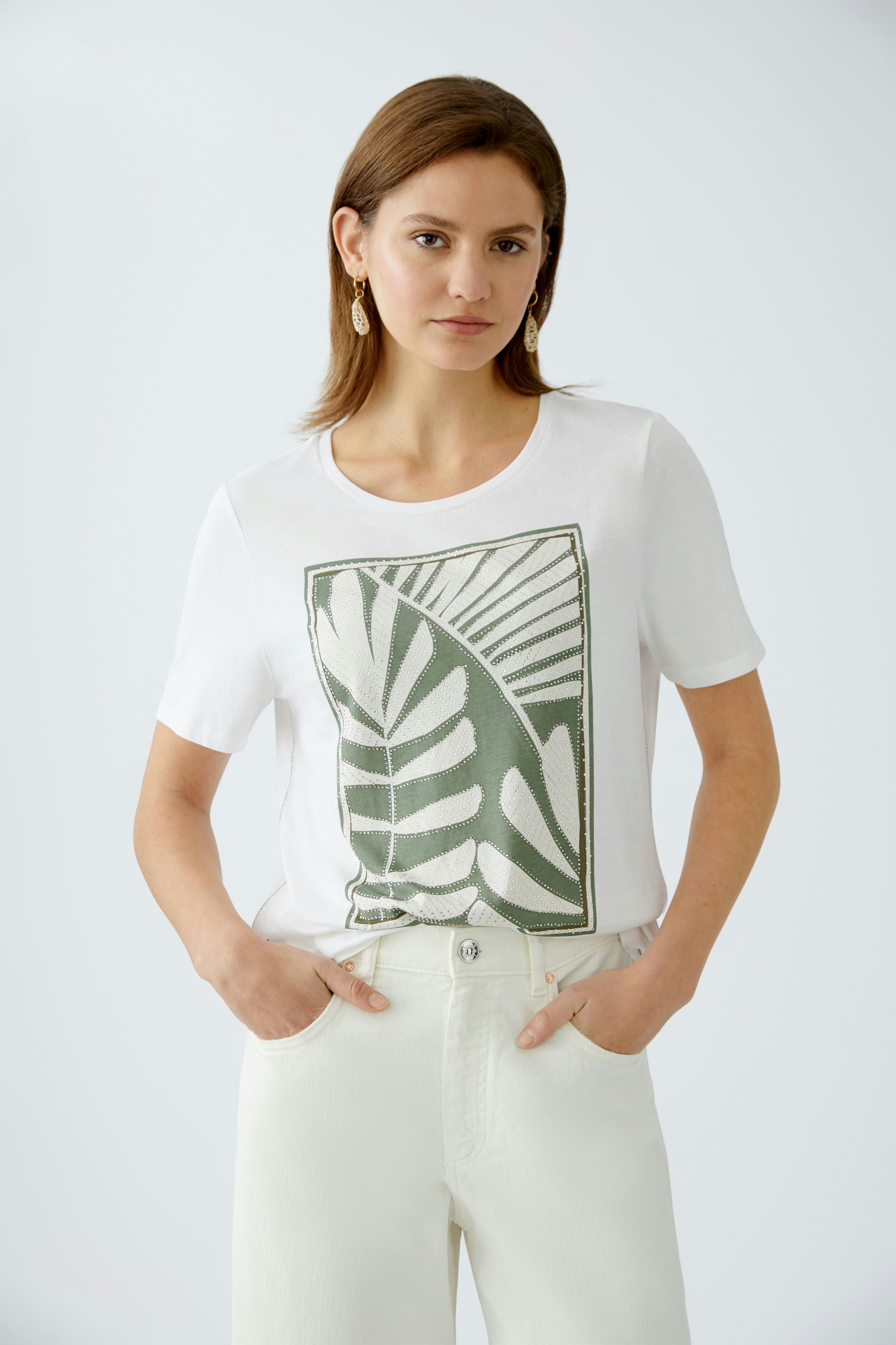 Stylish women's T-shirt: A woman in a white tee featuring a green leaf print, paired with light trousers.