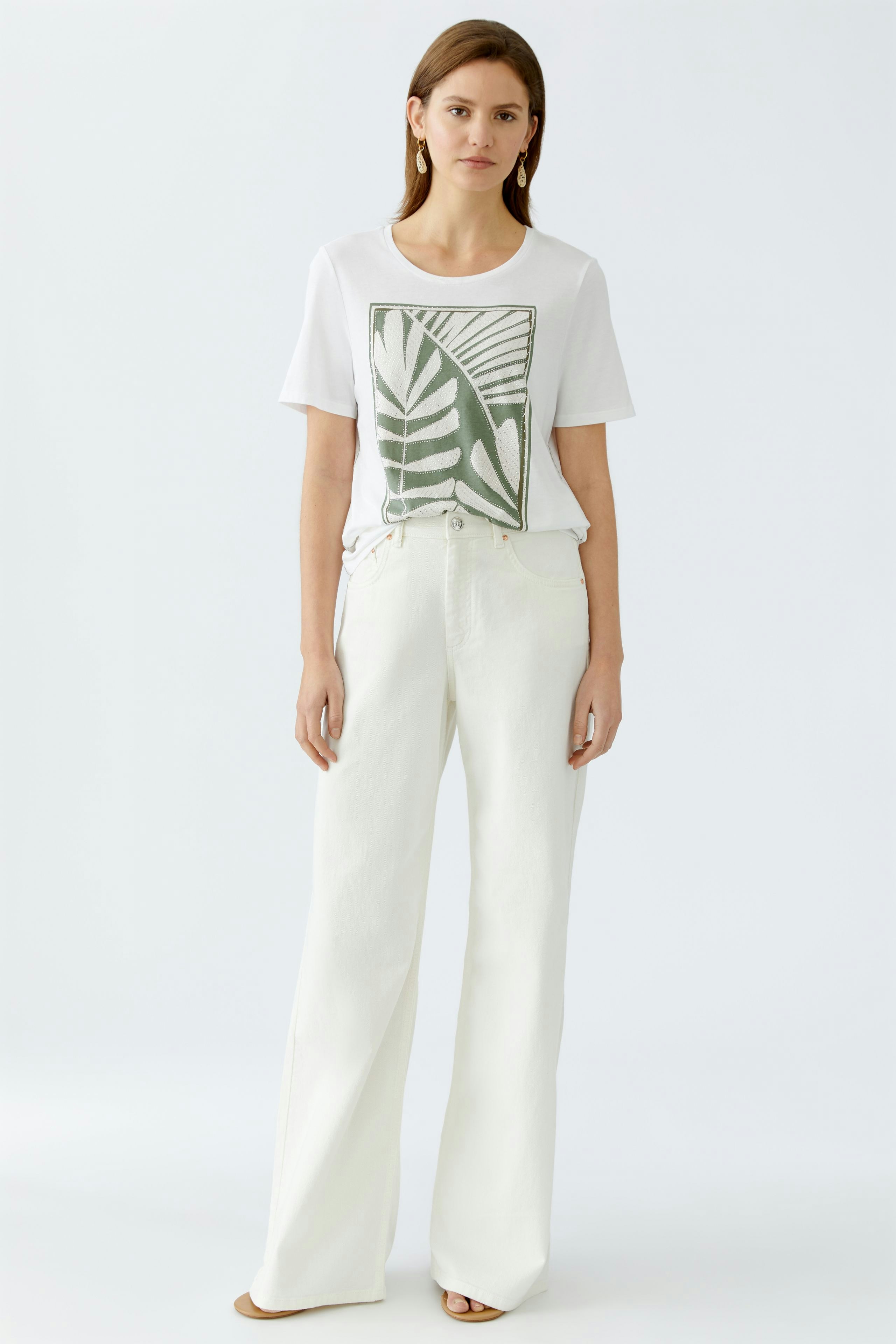 Stylish women's T-shirt: A woman in a white tee with a green leaf print, paired with wide-leg pants.