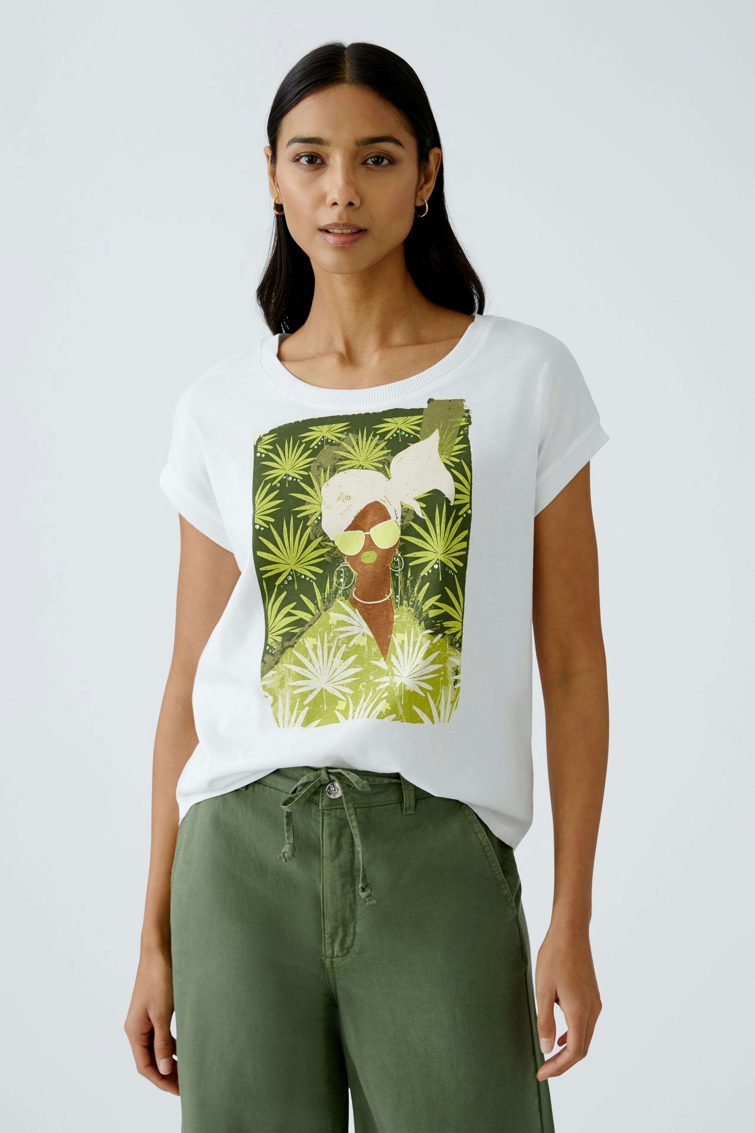 Stylish women's T-shirt: A woman in a white tee with a vibrant graphic design, paired with green pants.