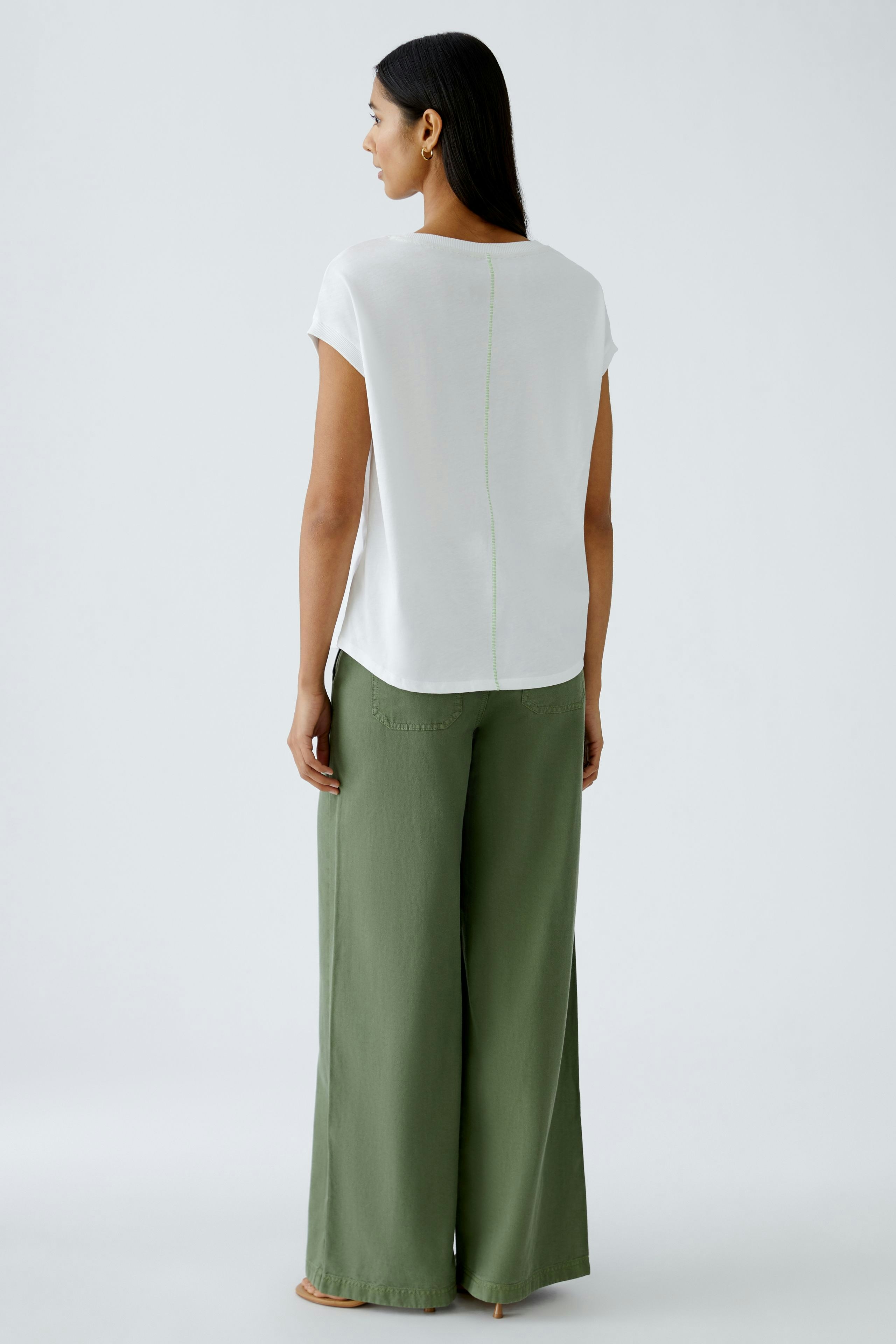 Stylish women's T-shirt: A woman in a white T-shirt with a subtle back seam, paired with green wide-leg pants.