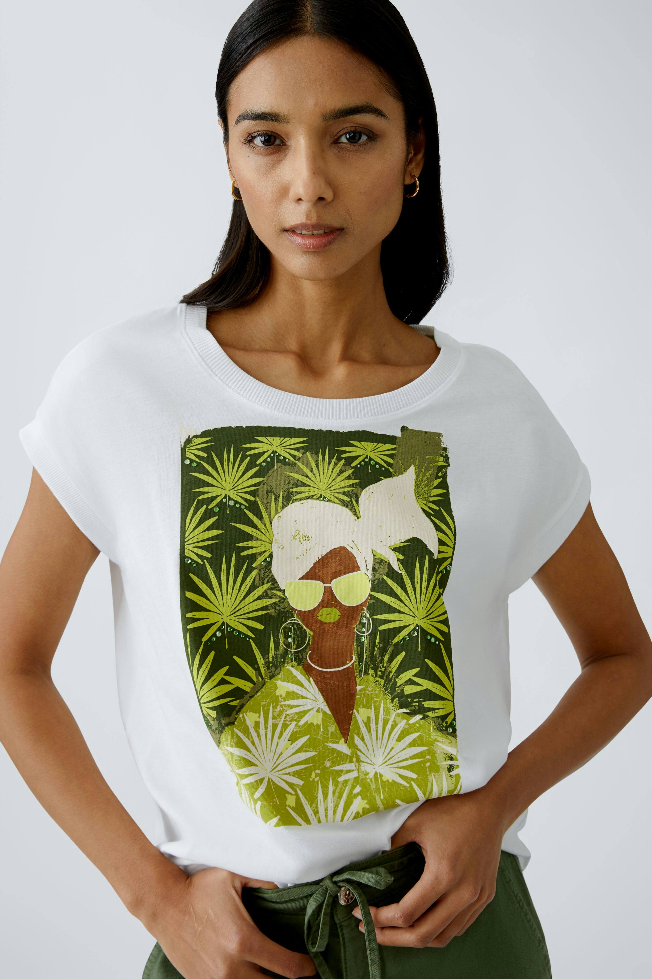 Stylish women's T-shirt: A woman in a white tee featuring a vibrant graphic design with tropical leaves.