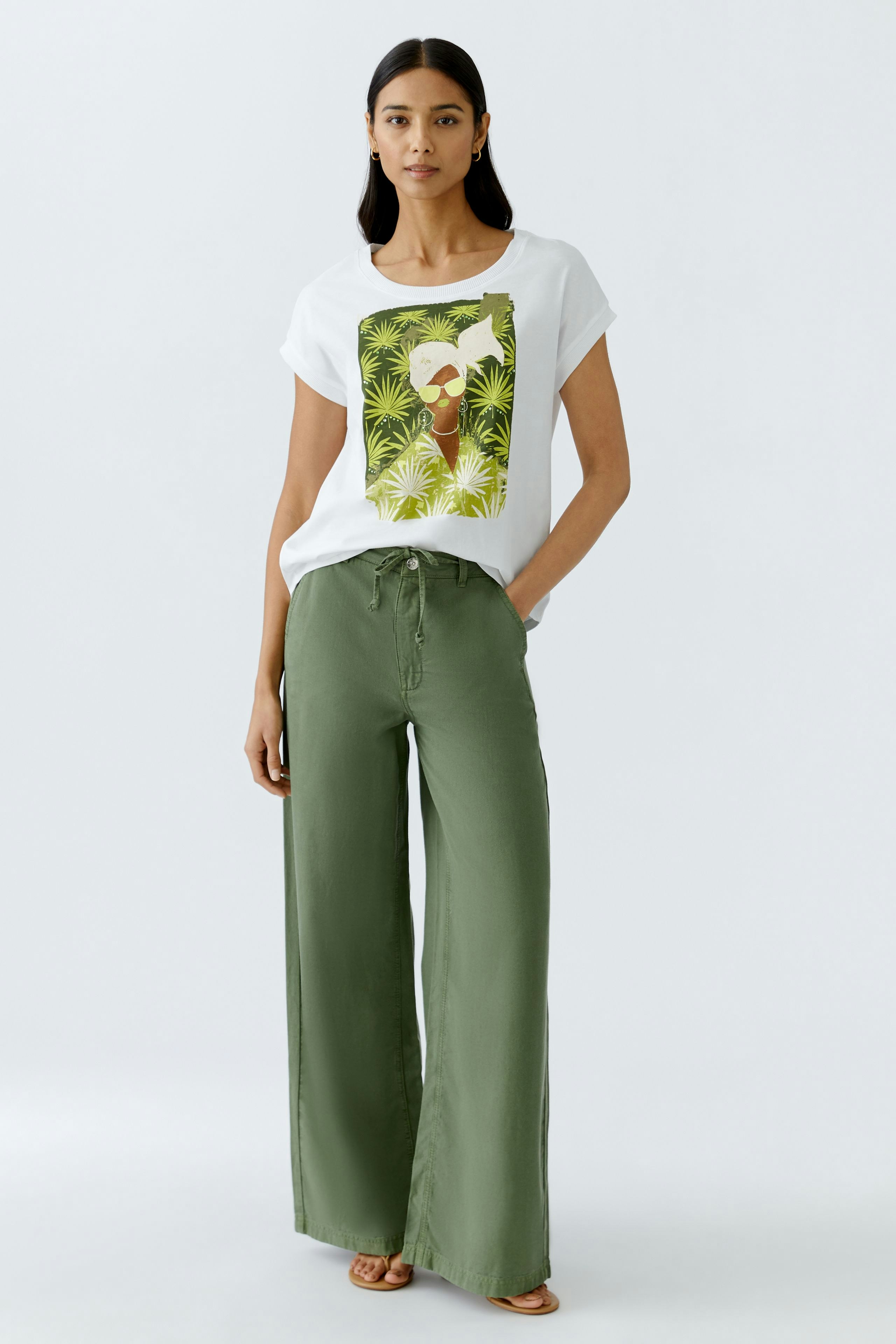 Stylish women's T-shirt featuring a vibrant graphic design, paired with relaxed green trousers.