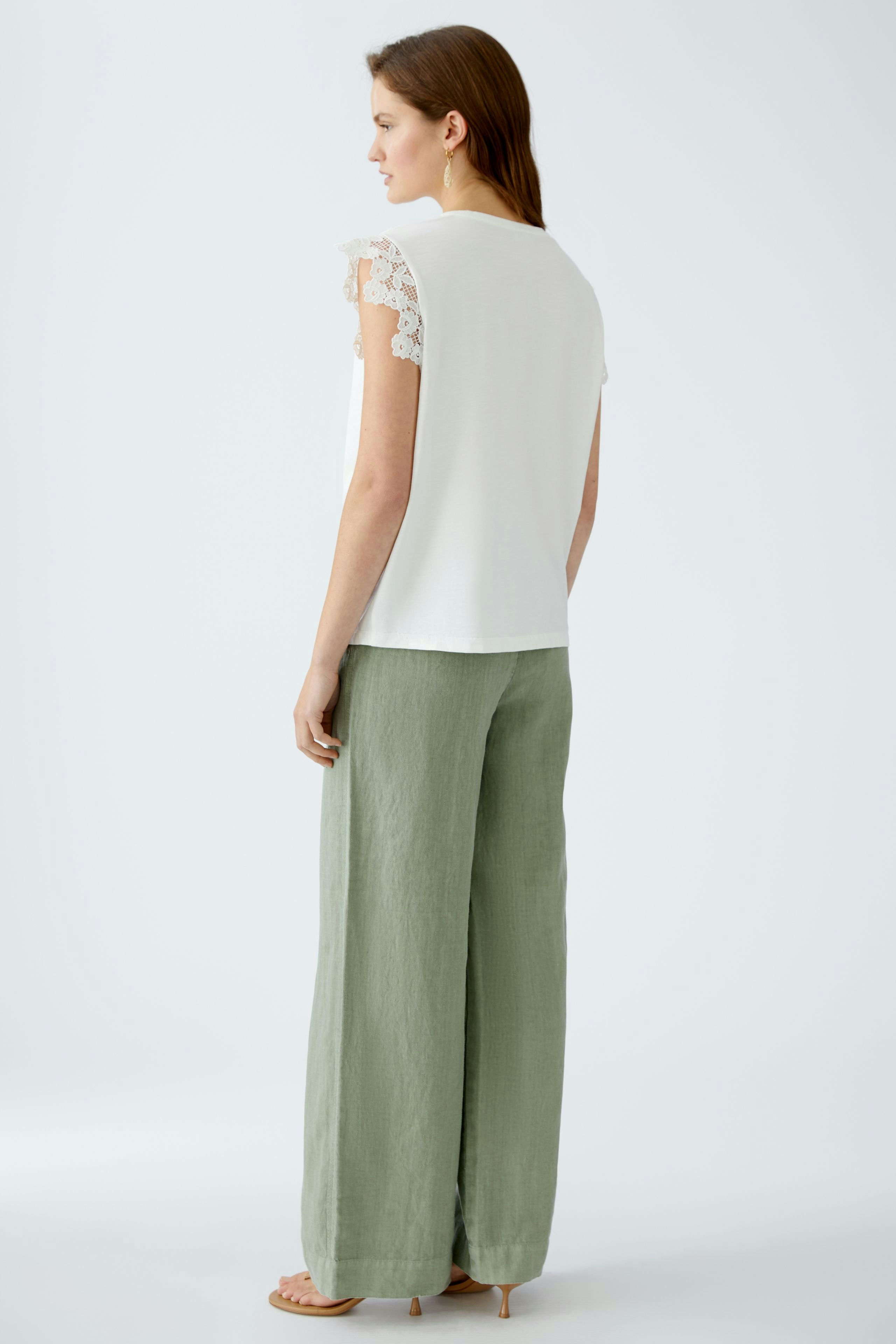 Elegantes Damen-Top: Frau in weißem Top mit Spitzenärmeln und lässiger Hose, ideal für den Sommer.