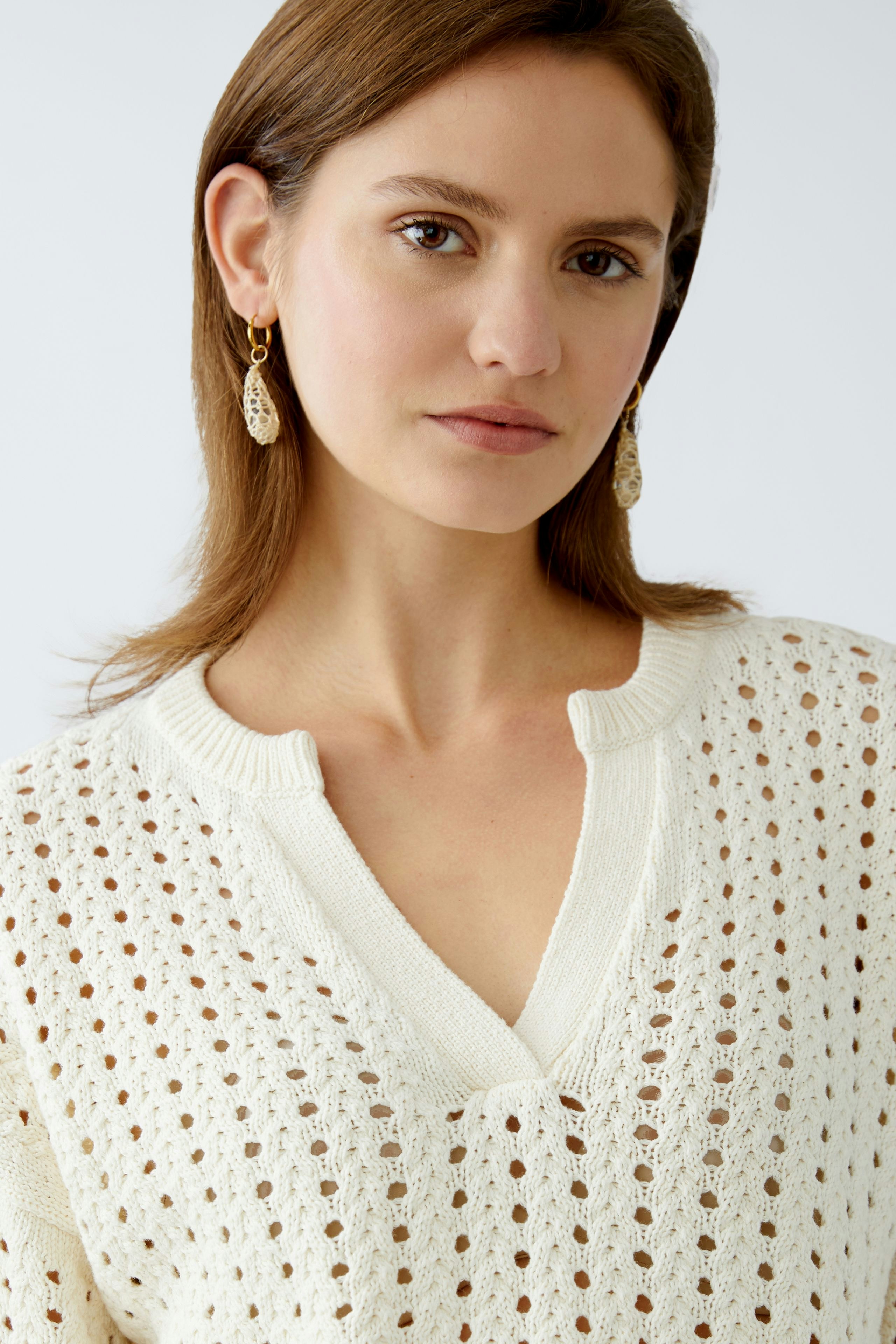 Stylish women's pullover: A woman in a cream-colored, open-knit pullover with a relaxed neckline.