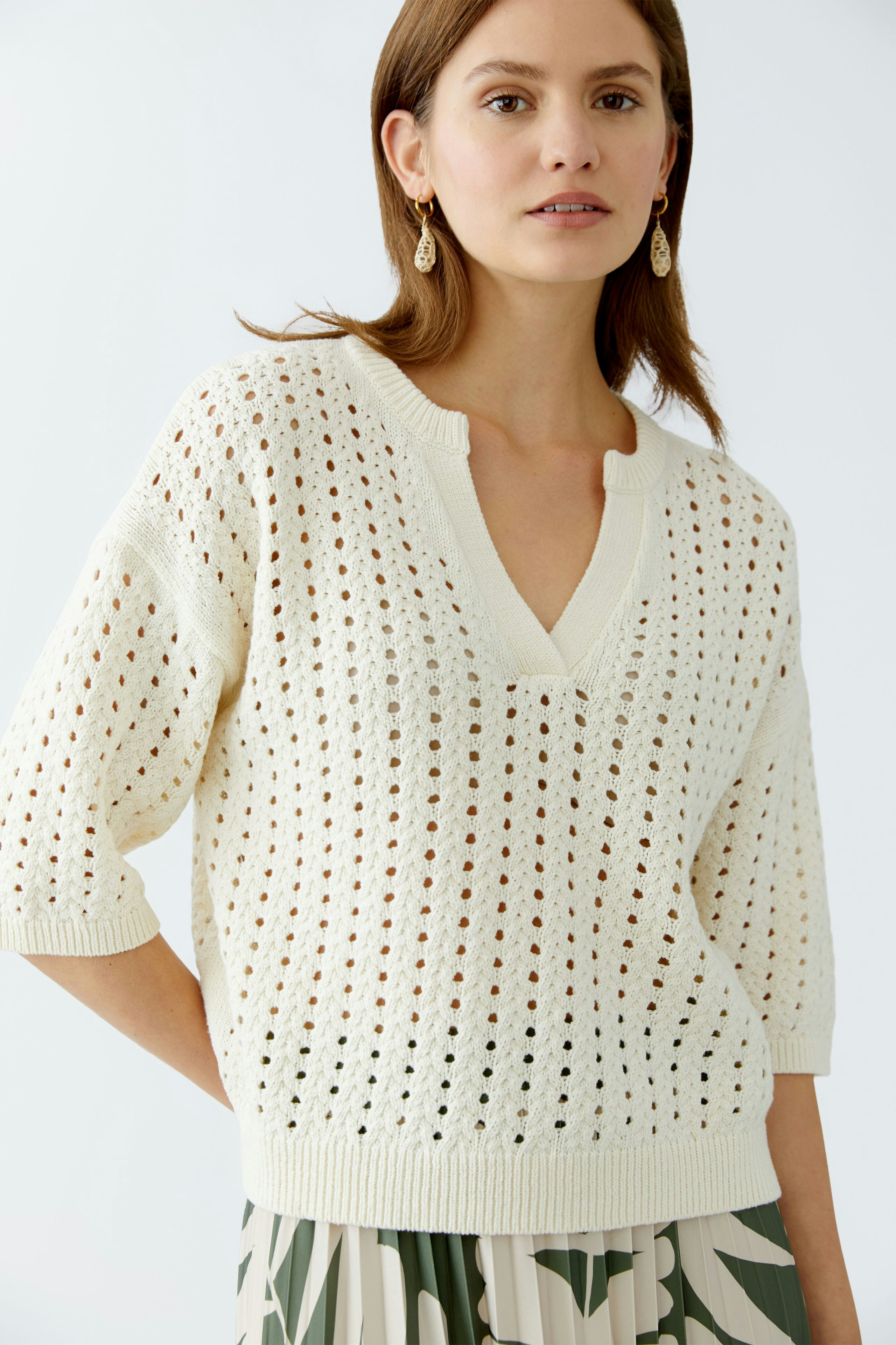 Stylish women's pullover: A woman in a cream open-knit pullover with a V-neck and relaxed fit.