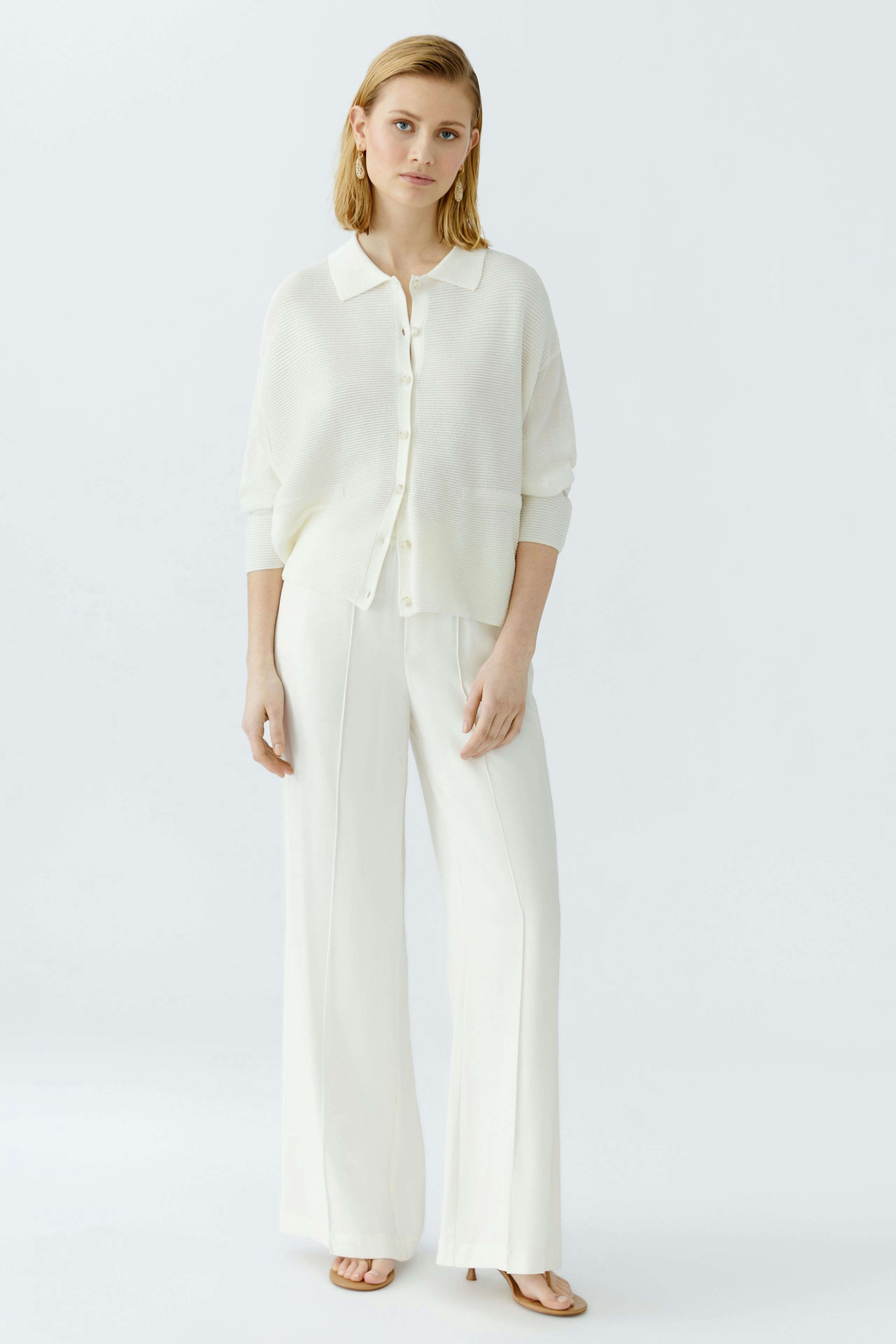 Elegant women's cardigan: A woman in a light cream cardigan paired with wide-leg trousers.