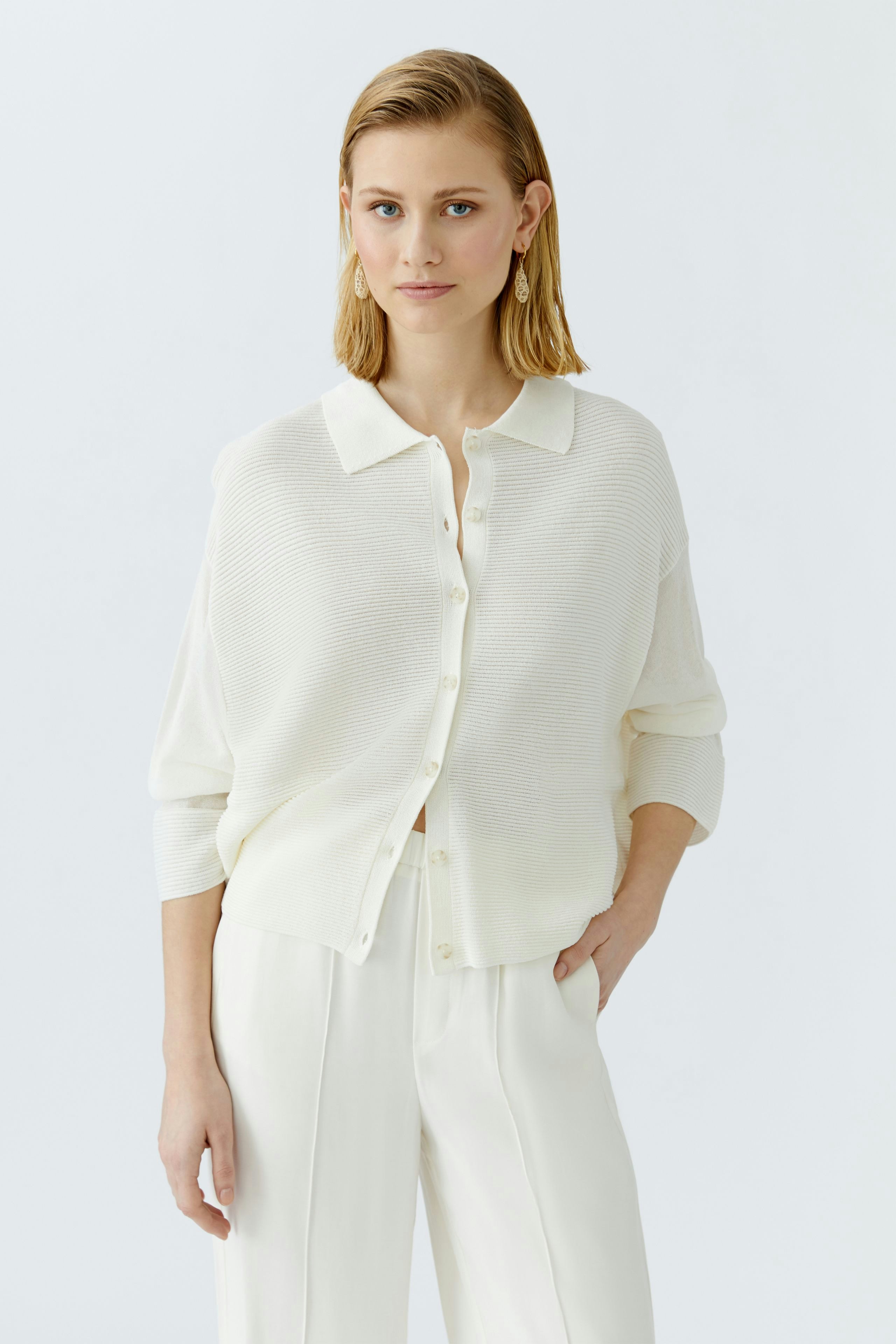 Stylish women's cardigan: A woman in a white cardigan with buttons, paired with elegant trousers.