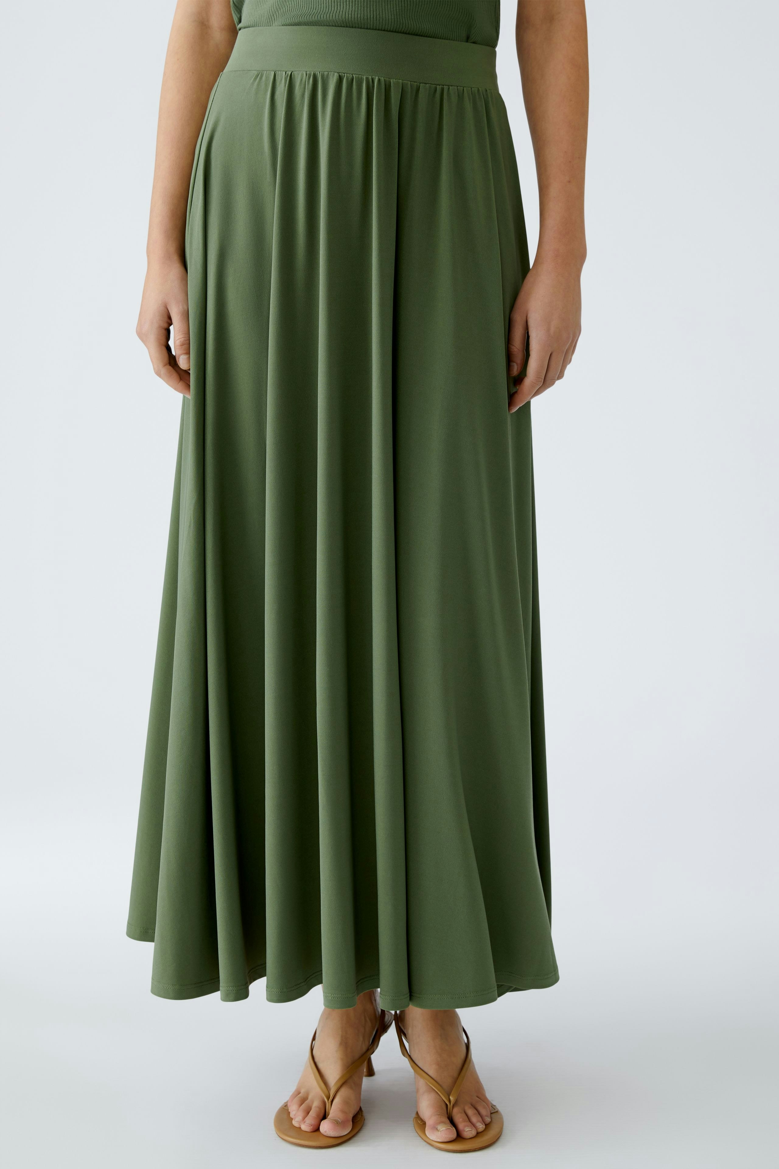 Eleganter A-Linien-Rock: Frau in einem langen, grünen Rock mit fließendem Stoff und lässigen Sandalen.