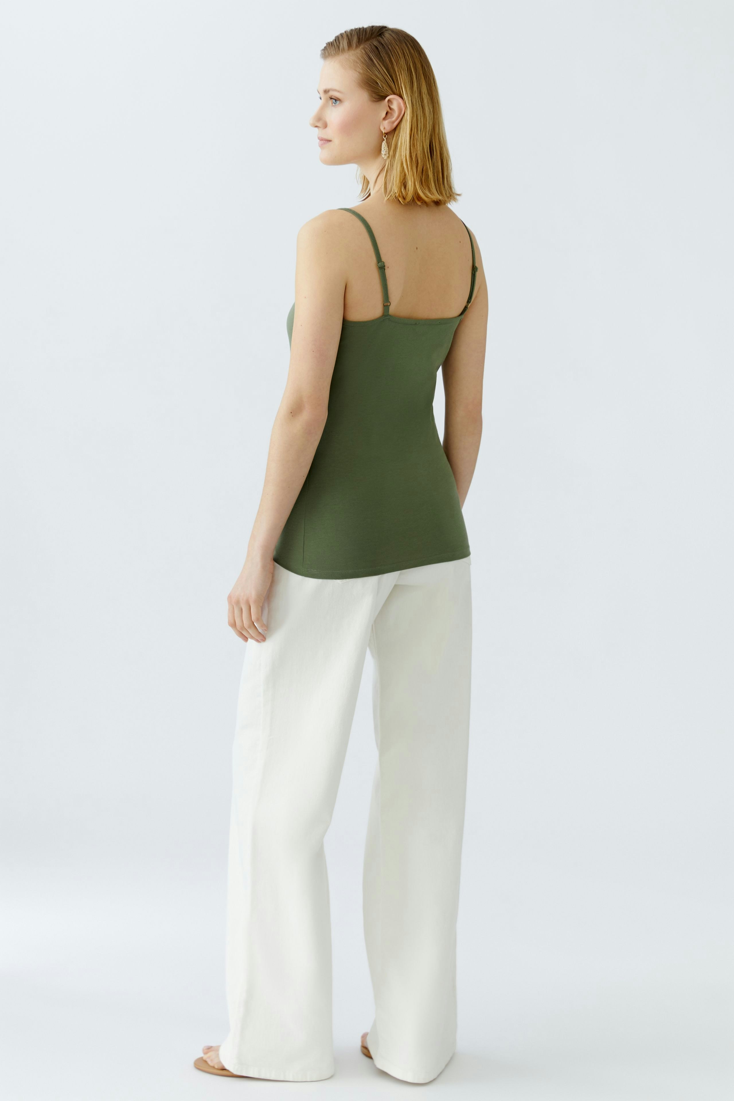 Elegantes Damen-Top: Frau in grünem Top mit schmalen Trägern und weißen, weiten Hosen.
