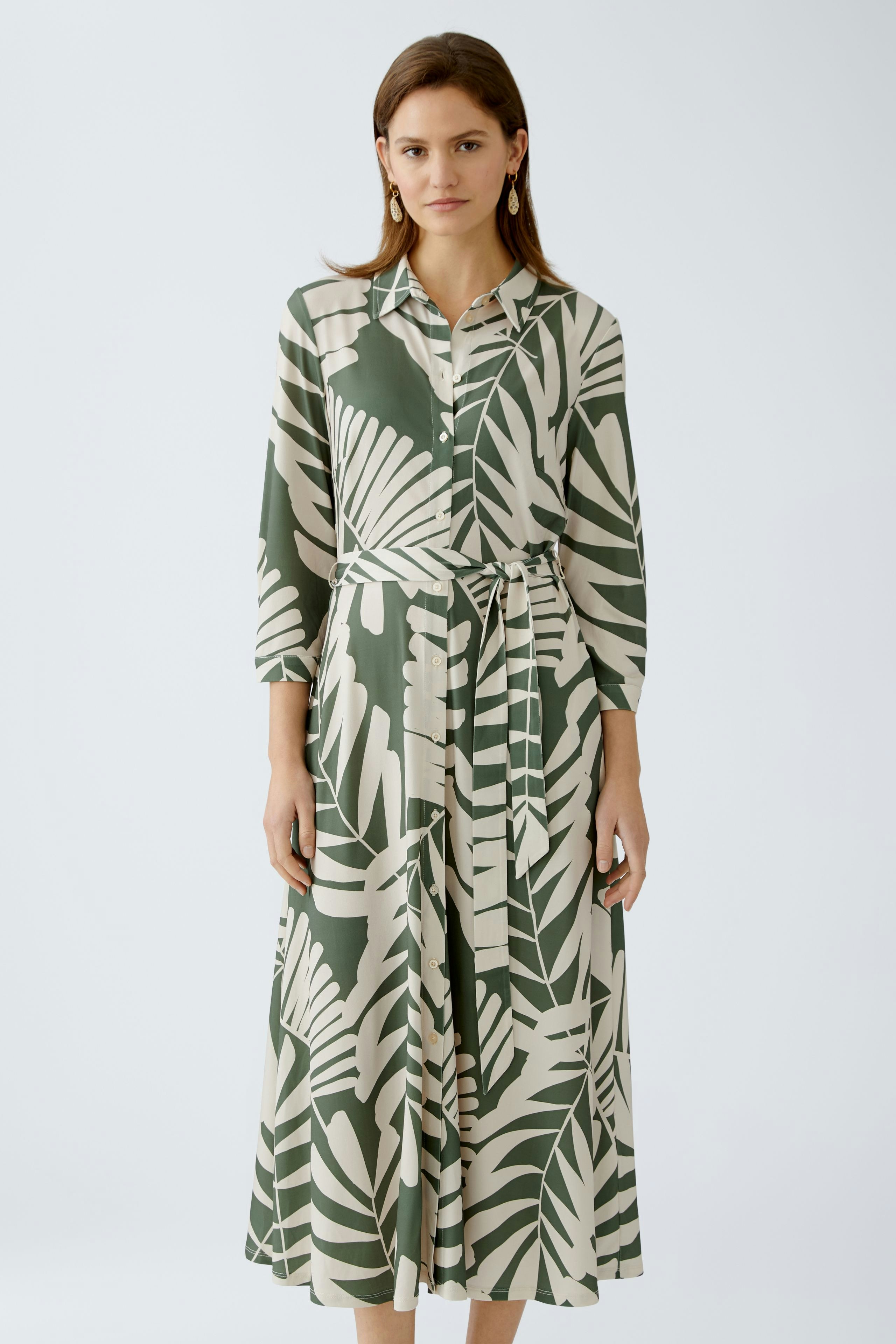 Hemdblusenkleid: Frau in einem eleganten, gemusterten Kleid mit Gürtel und langen Ärmeln.